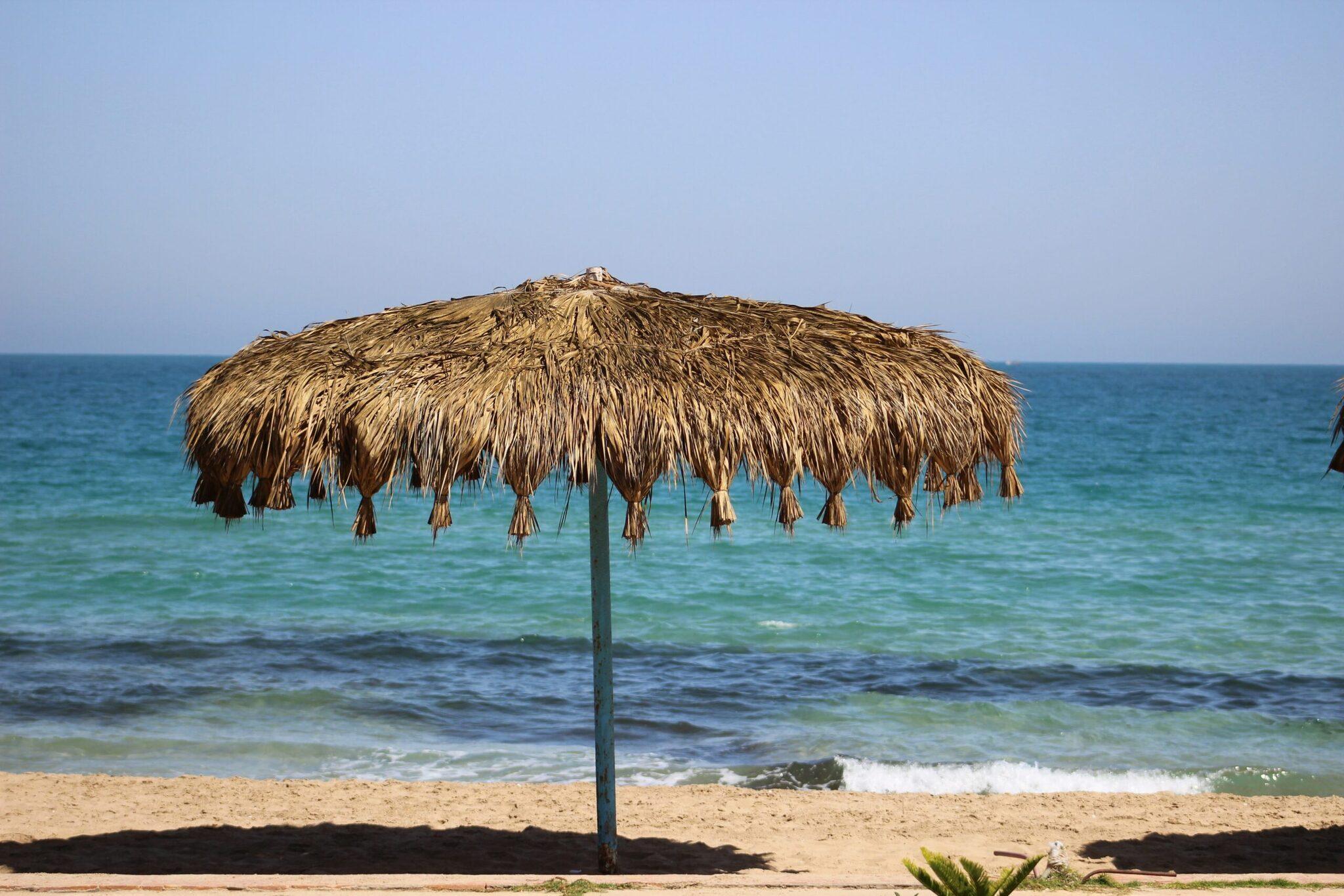 Un parasol en paille tressée sur une plage de sable face à la mer turquoise et calme