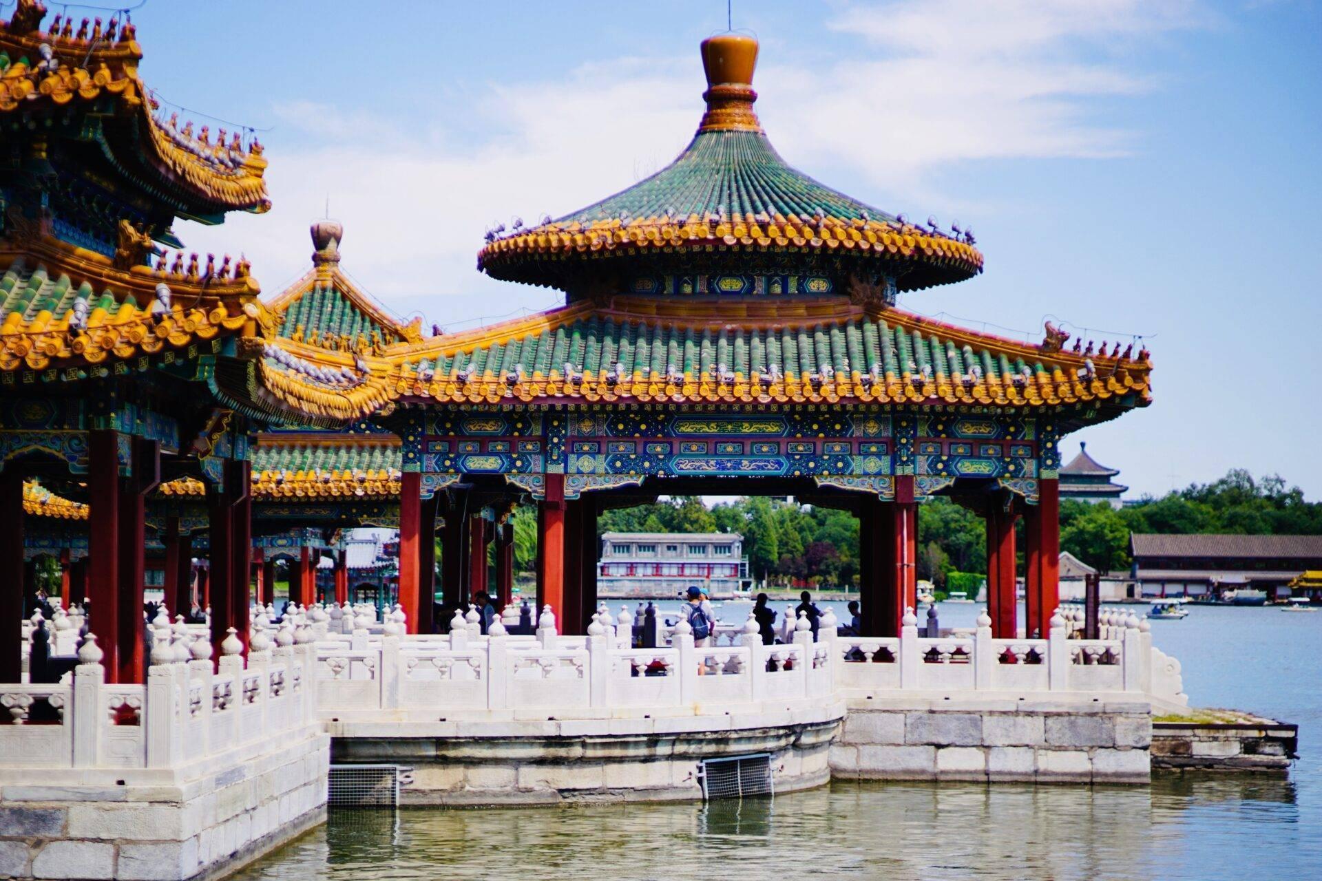 Un pavillon traditionnel chinois aux toits dorés et verts surplombant un lac avec des balustrades blanches