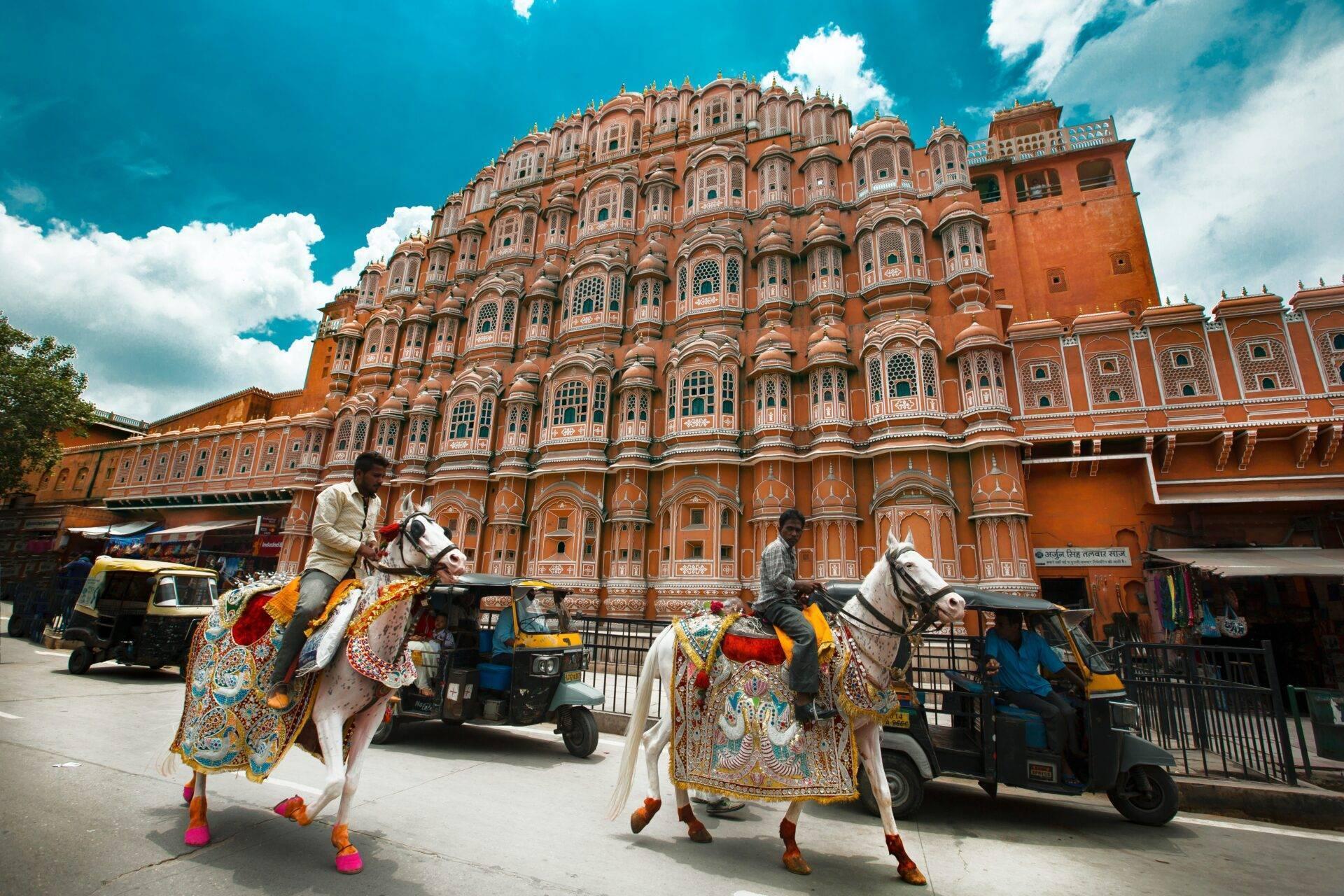 Two riders on ornately decorated horses pose before an elaborate pink palace