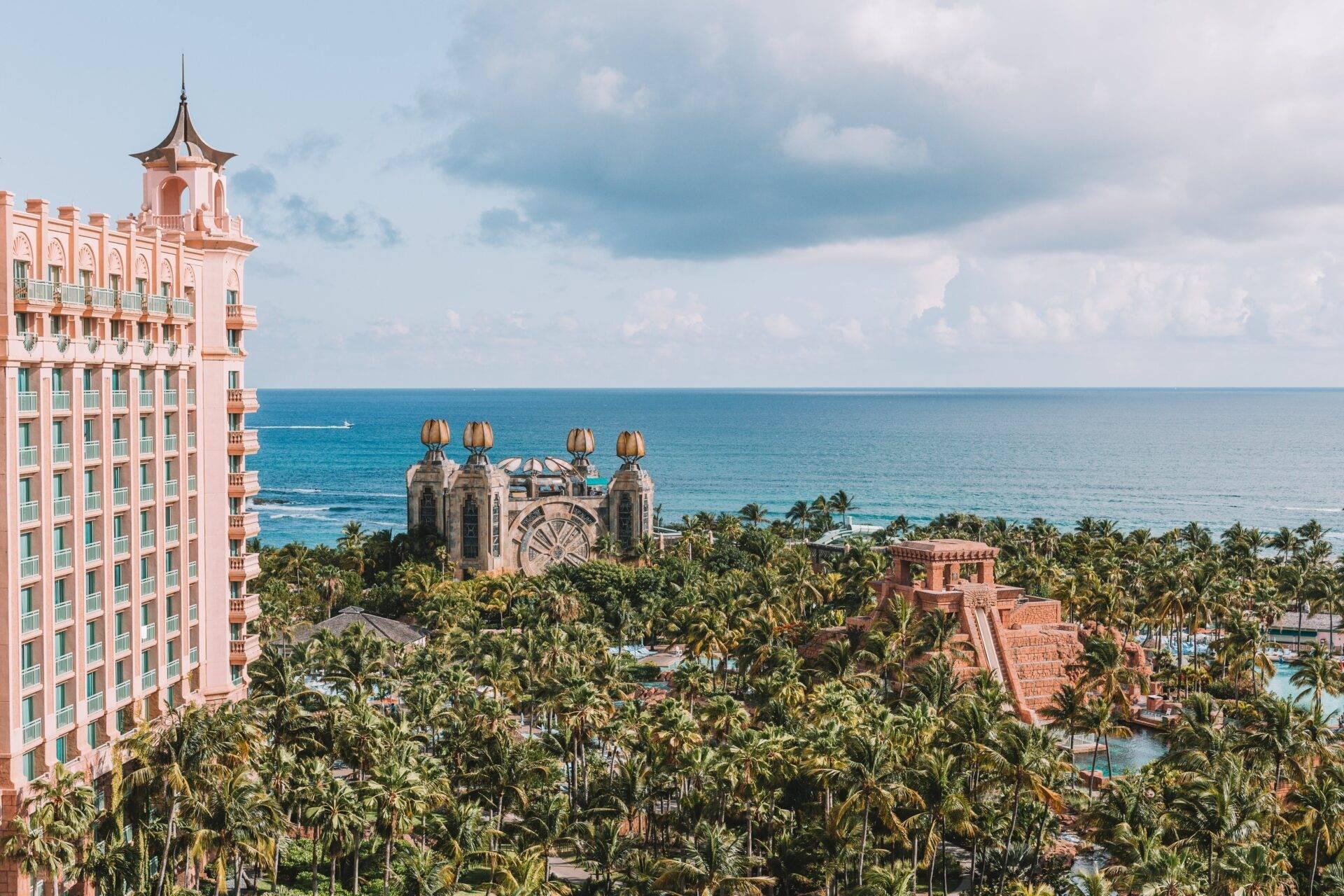 Vue aérienne d’un complexe hôtelier luxueux avec architecture rose, palmiers tropicaux et plage turquoise aux Bahamas