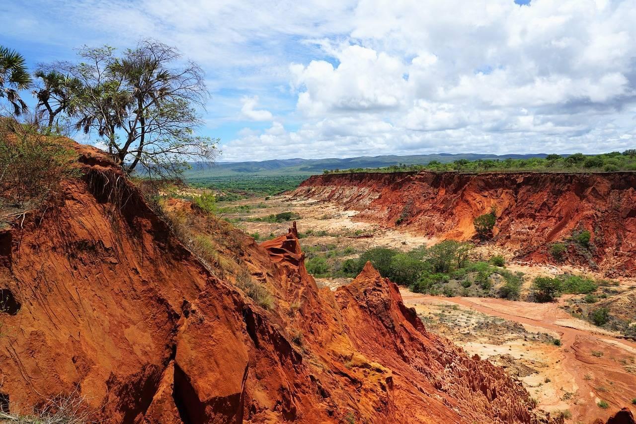 Laterite quarry with striking red rock formations rising above a green valley under a cloudy sky