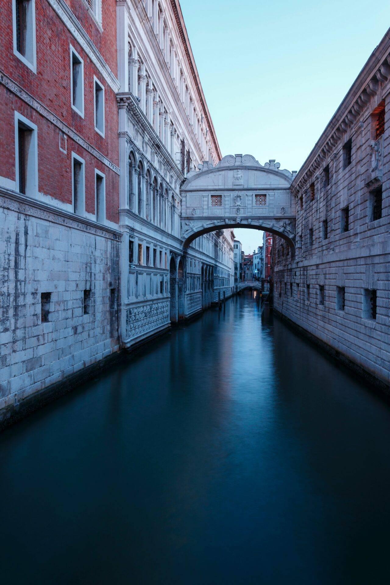 A Venetian canal at dusk with the famous Bridge of Sighs linking two historic stone palaces
