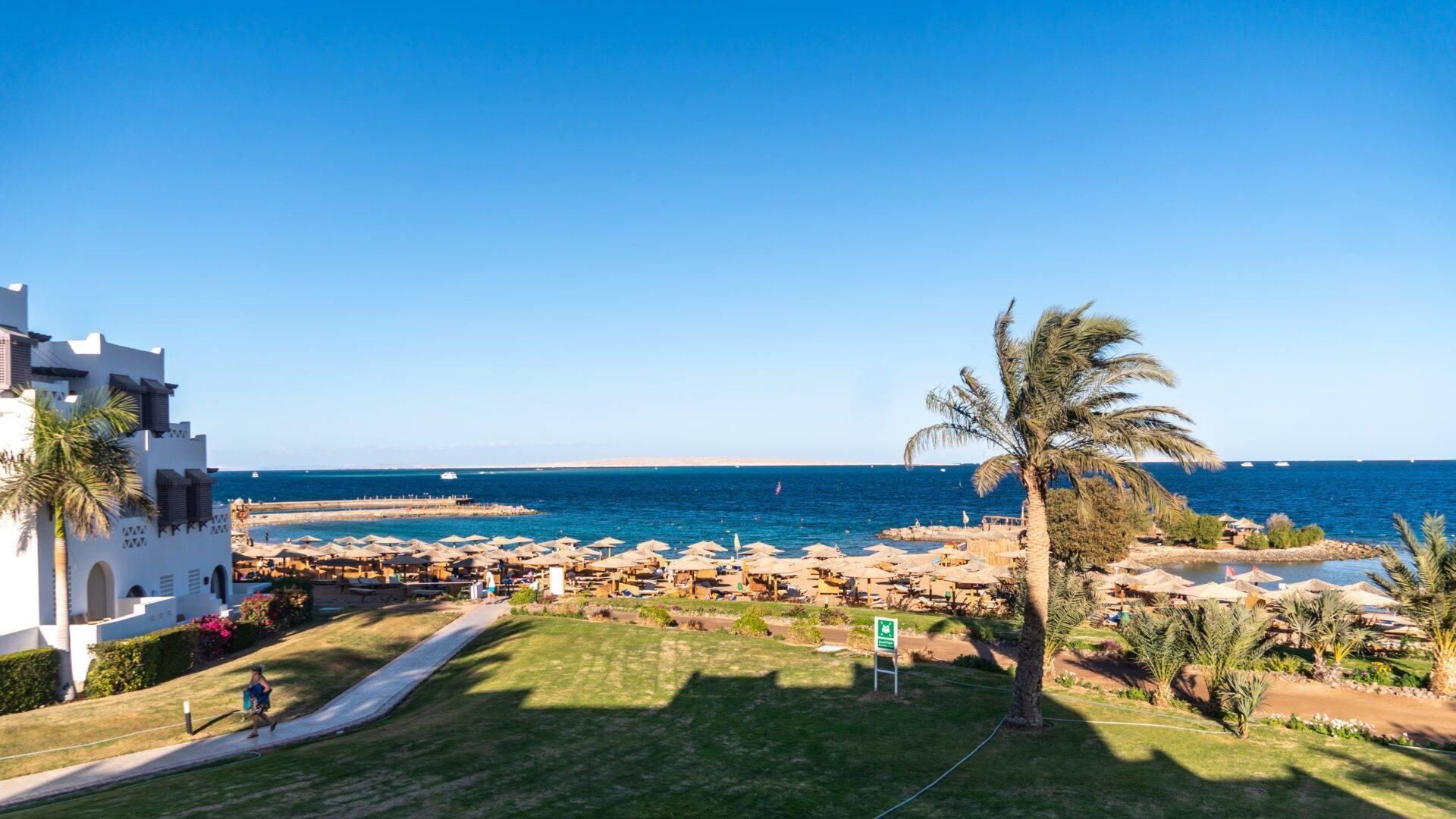 Aerial view of a beach resort with sandy shores, palm trees and white architecture overlooking turquoise water