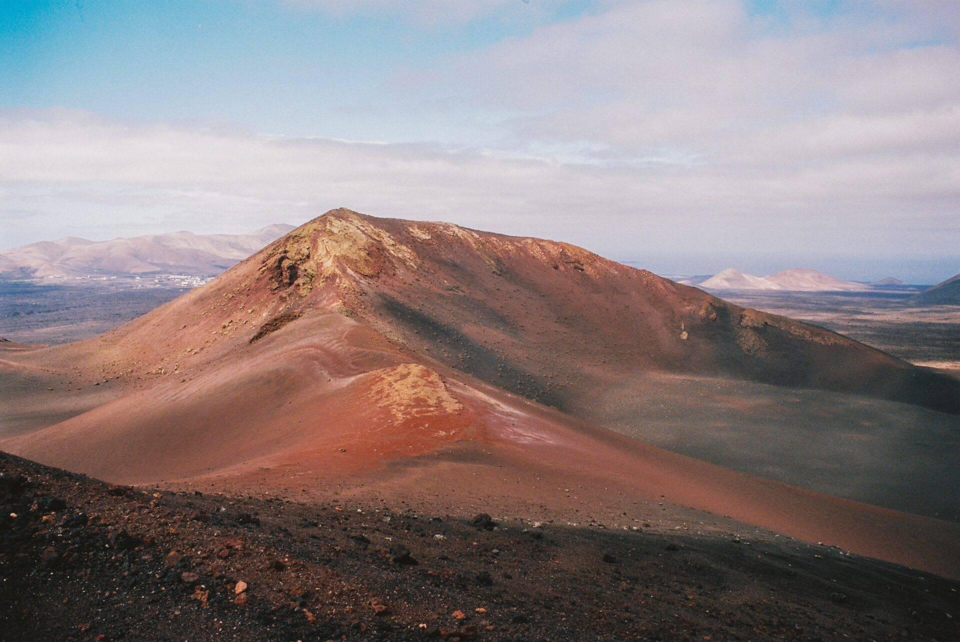 Volcan aux pentes rougeâtres et noires dominando un paysage aride de montagne désertique sous ciel dégagé