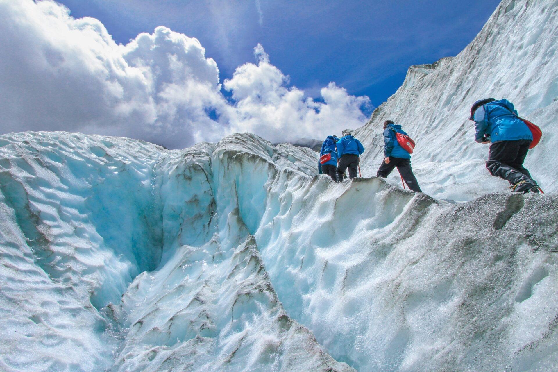 Un groupe de randonneurs traverse un glacier bleu spectaculaire sous un ciel dégagé et ensoleillé
