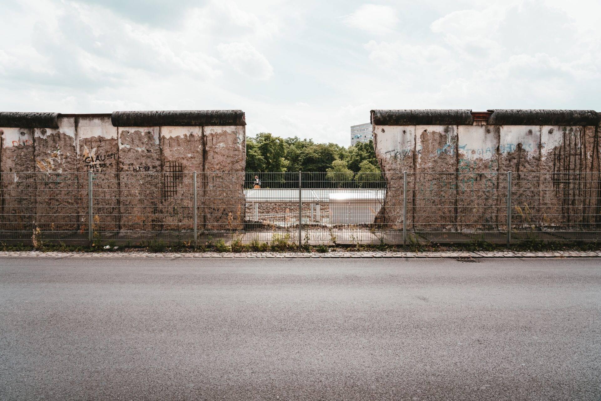 Remains of the Berlin Wall with exposed brickwork, graffiti and a metal fence, on an overcast day