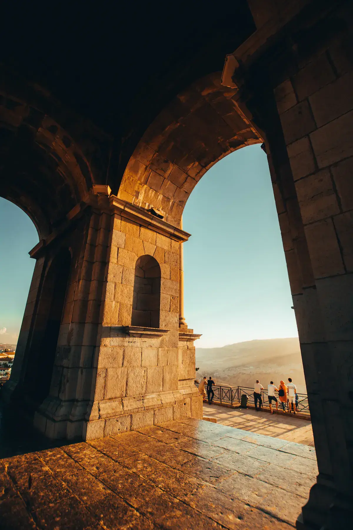 Des ruines de pierre avec arcs majestueux surplombant un paysage montagneux désertique au coucher de soleil