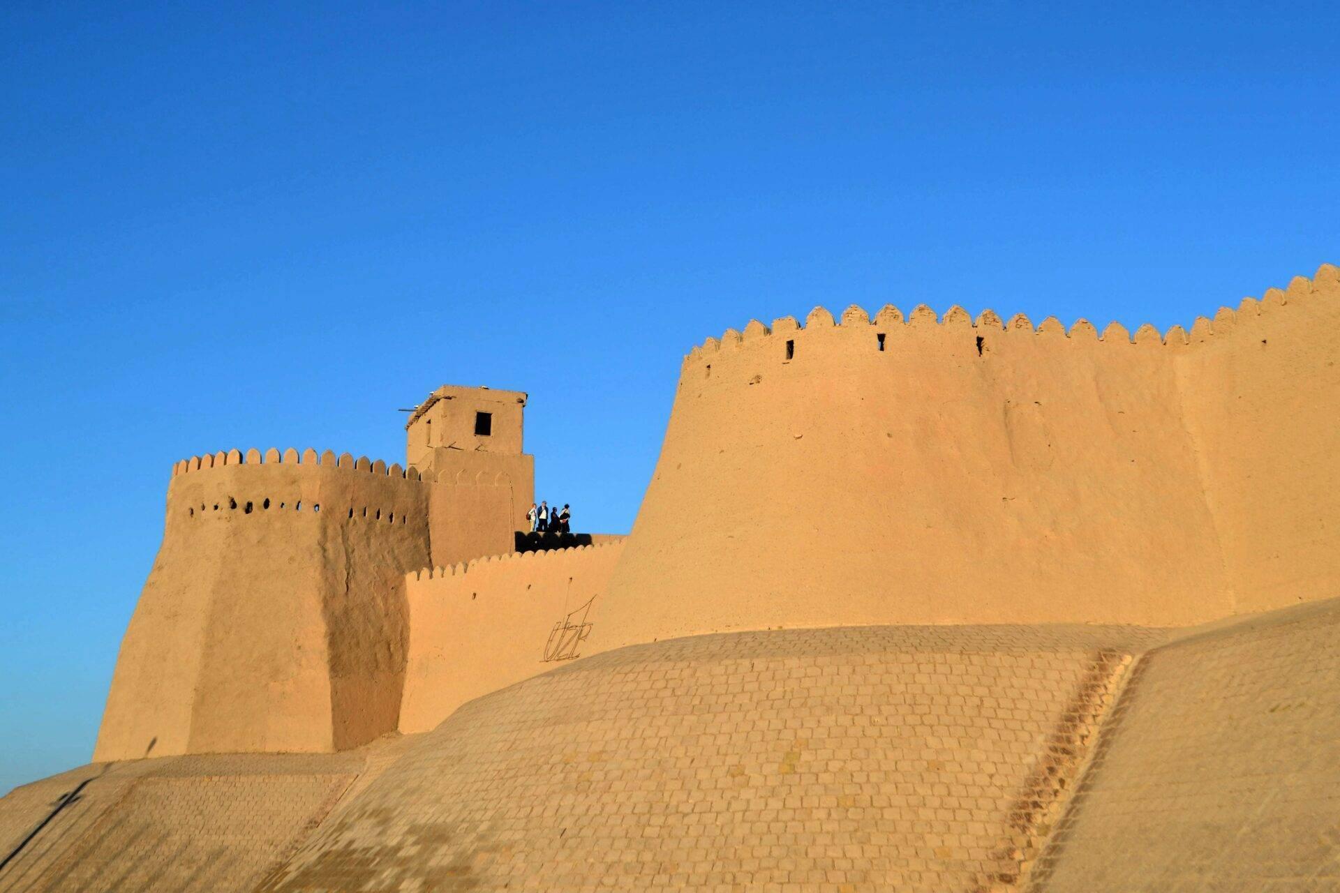 A historic adobe fortress with crenellated ramparts under a clear blue sky