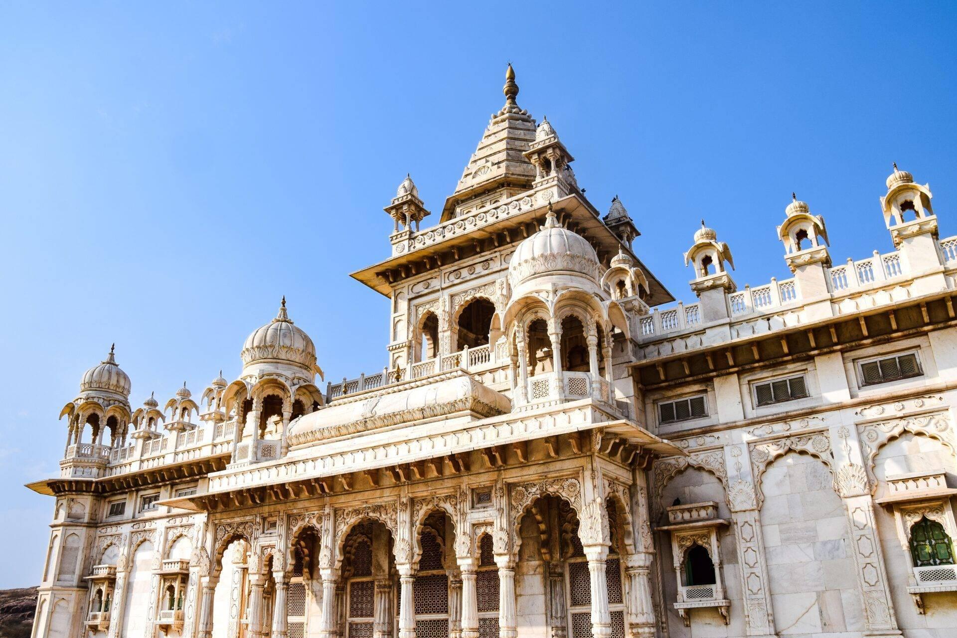 A white and gold Hindu temple with domes and ornamental turrets under a clear blue sky