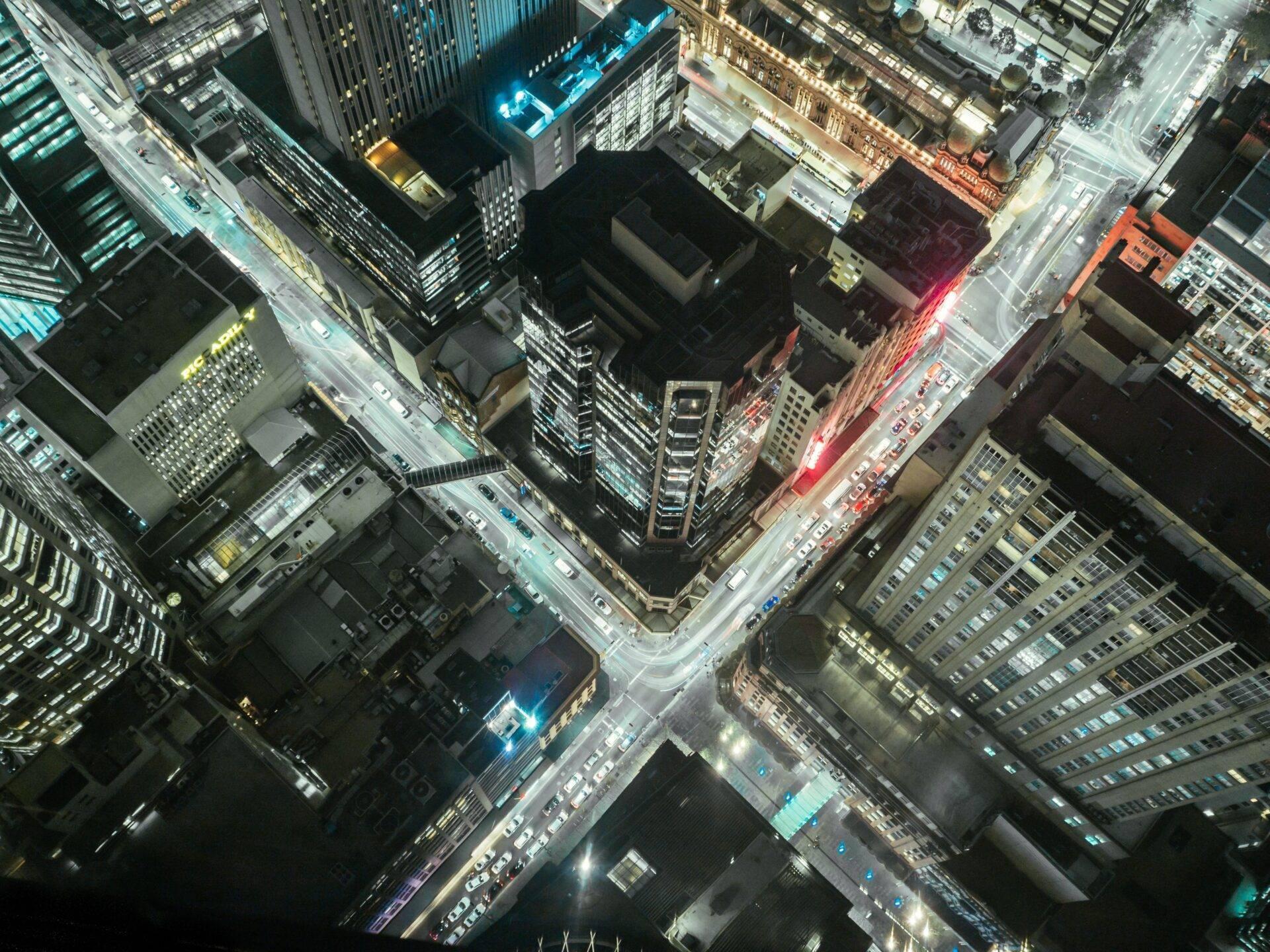 Vue aérienne nocturne d’une intersection urbaine animée avec immeubles éclairés et circulation routière