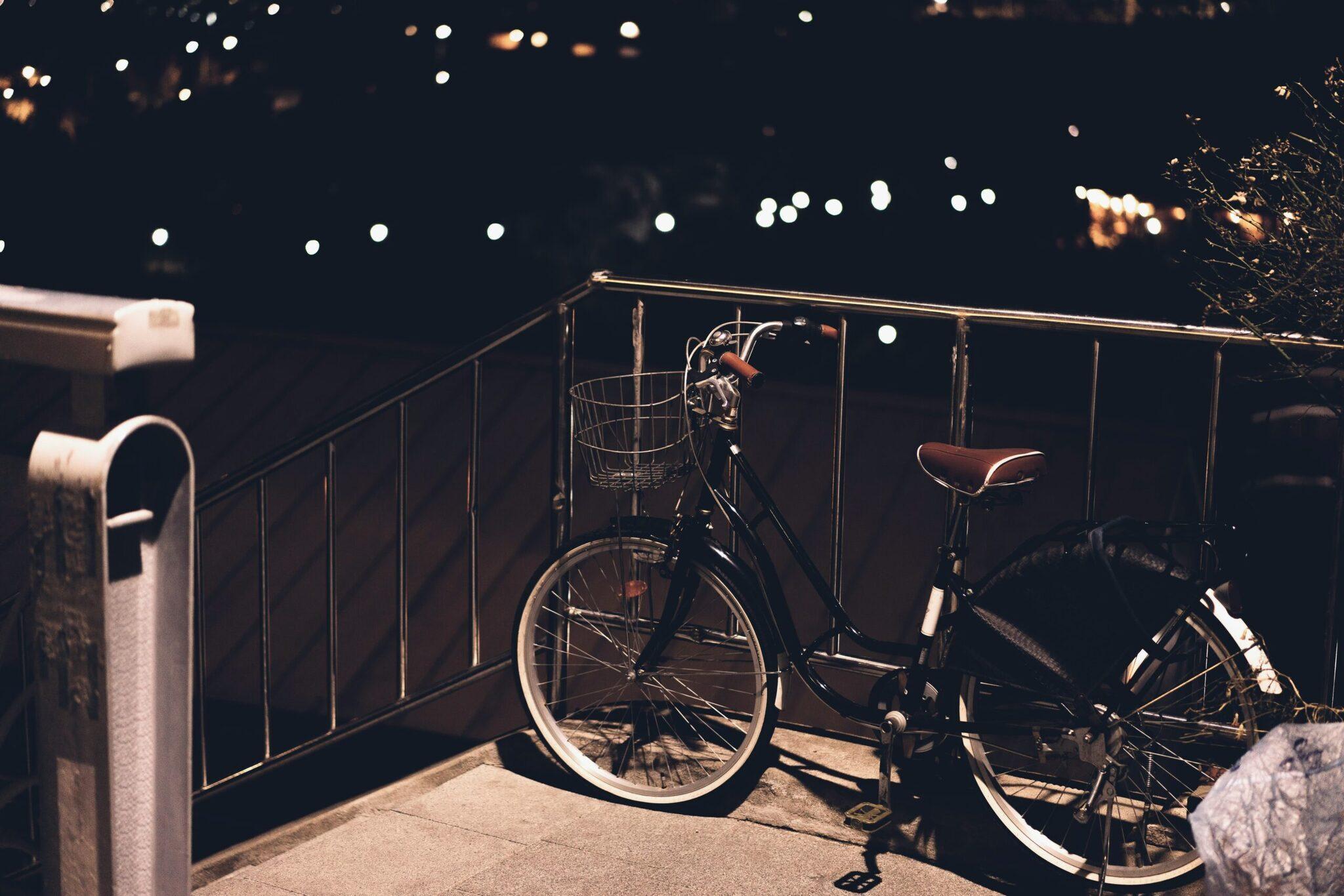 Two bicycles parked against a metal railing at night with city lights in the background