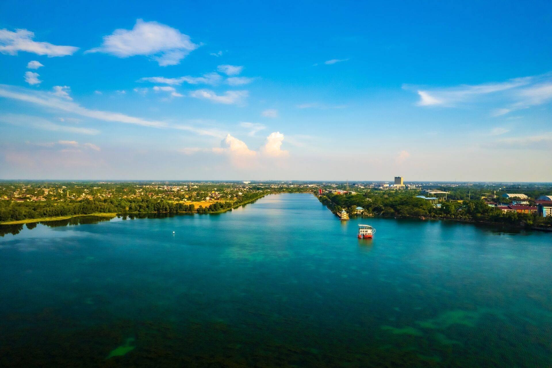 Aerial view of a turquoise river bordered by tropical vegetation with a tourist boat and a coastal town in the distance