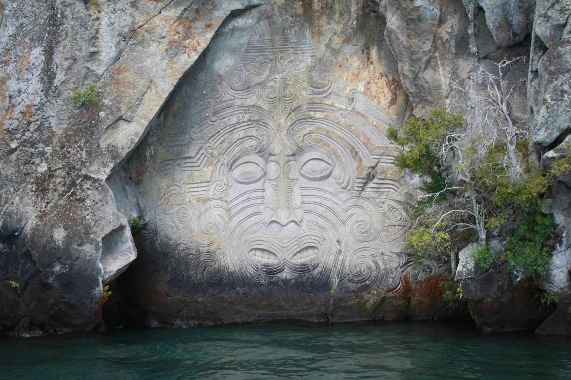 Carving maori gravé dans la roche surplombant une eau turquoise en Nouvelle-Zélande