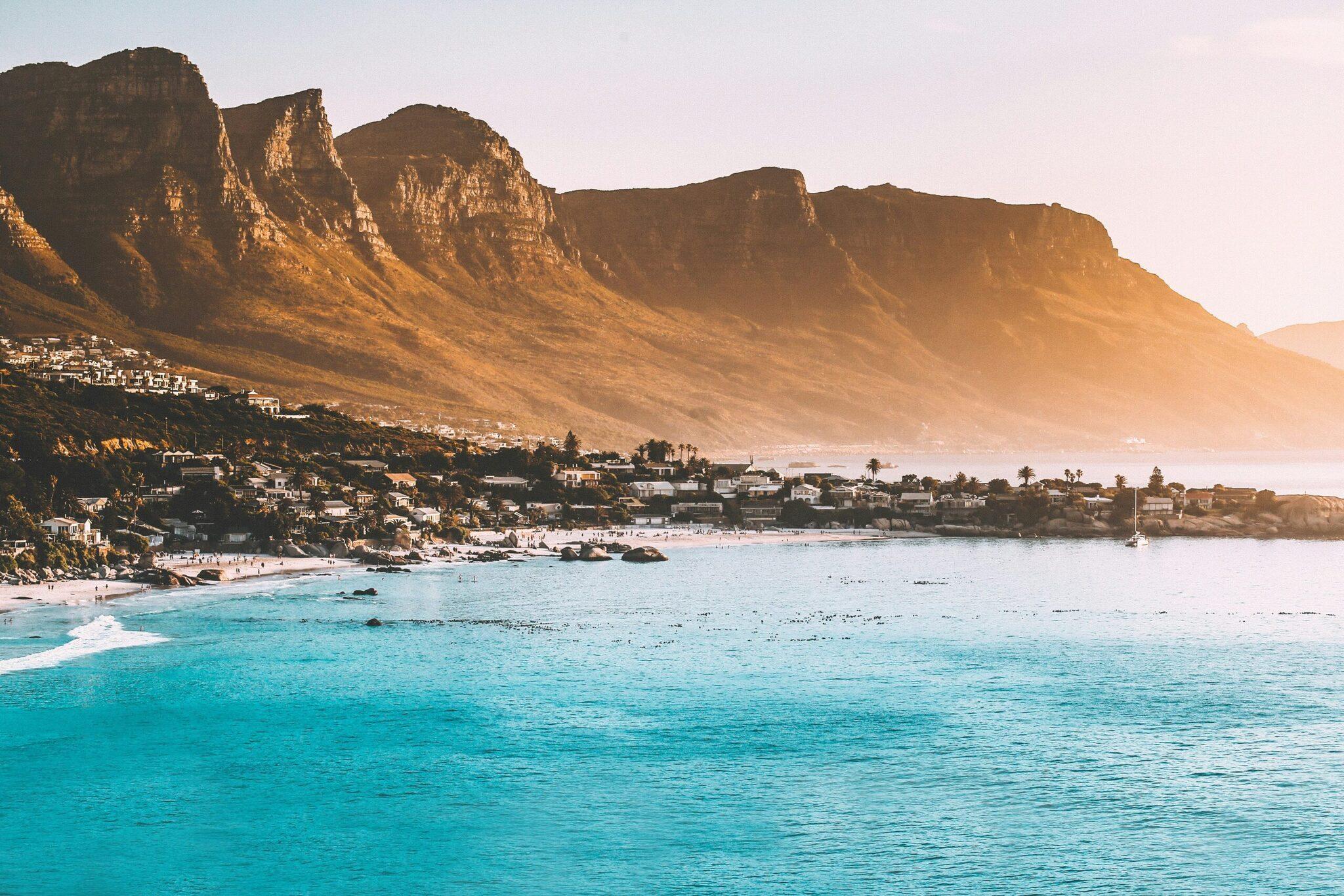 A white-sand beach with turquoise waters facing steep rocky mountains and a coastal town