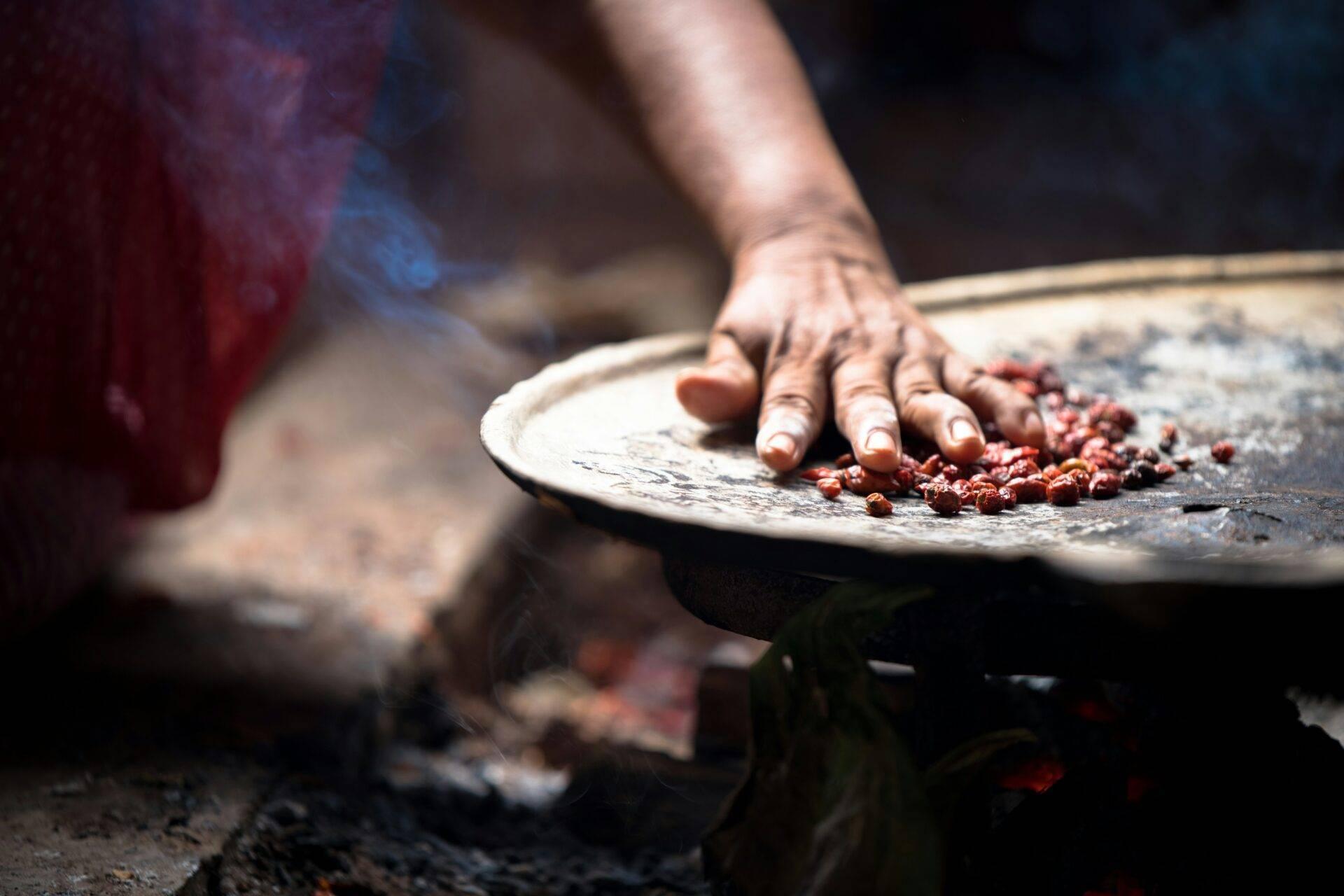 Une main qui moud des grains de cacao rouges sur une surface plate traditionnelle au Guatemala