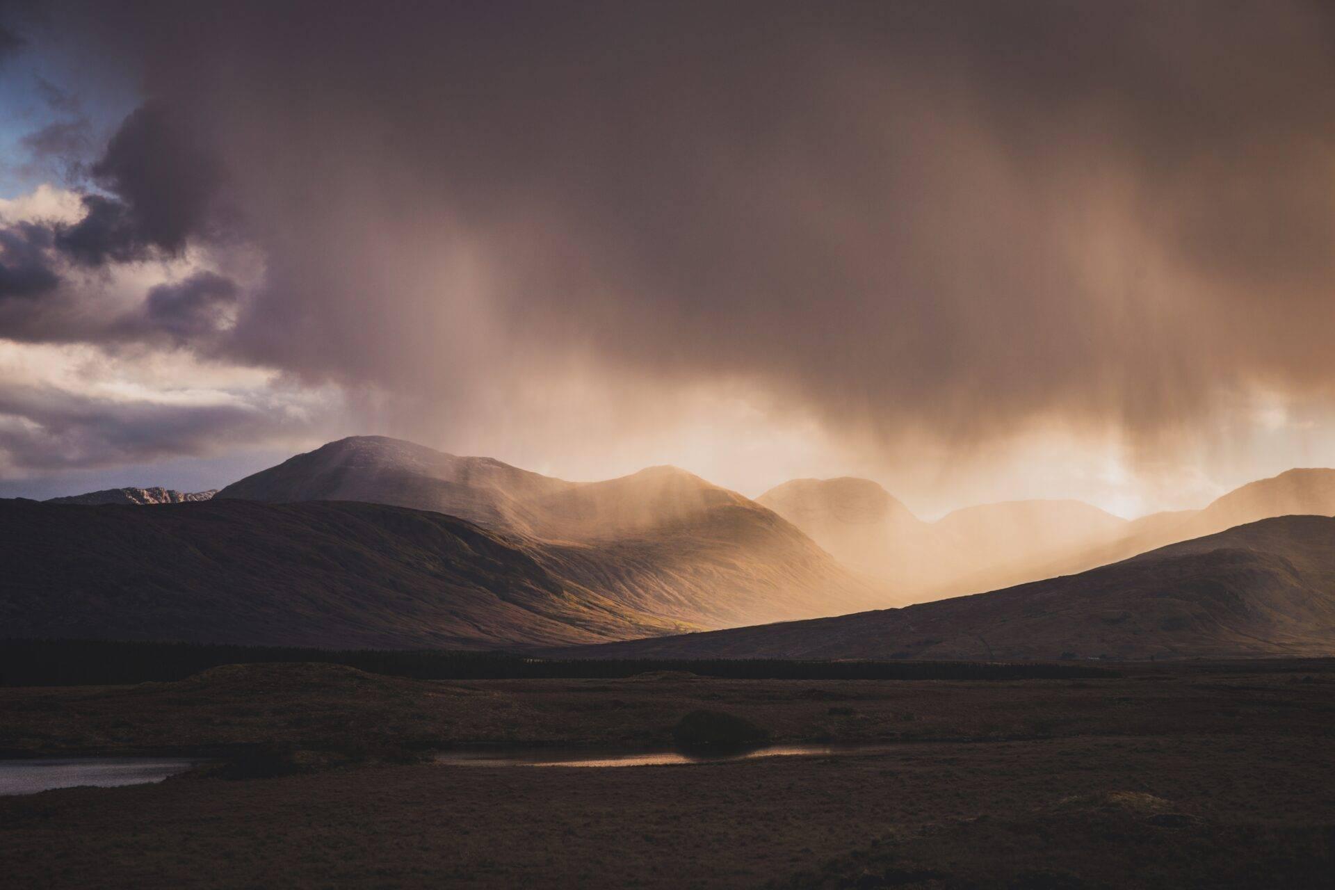 Barren mountains bathed in golden light with a dramatic cloudy sky and a river in the valley below