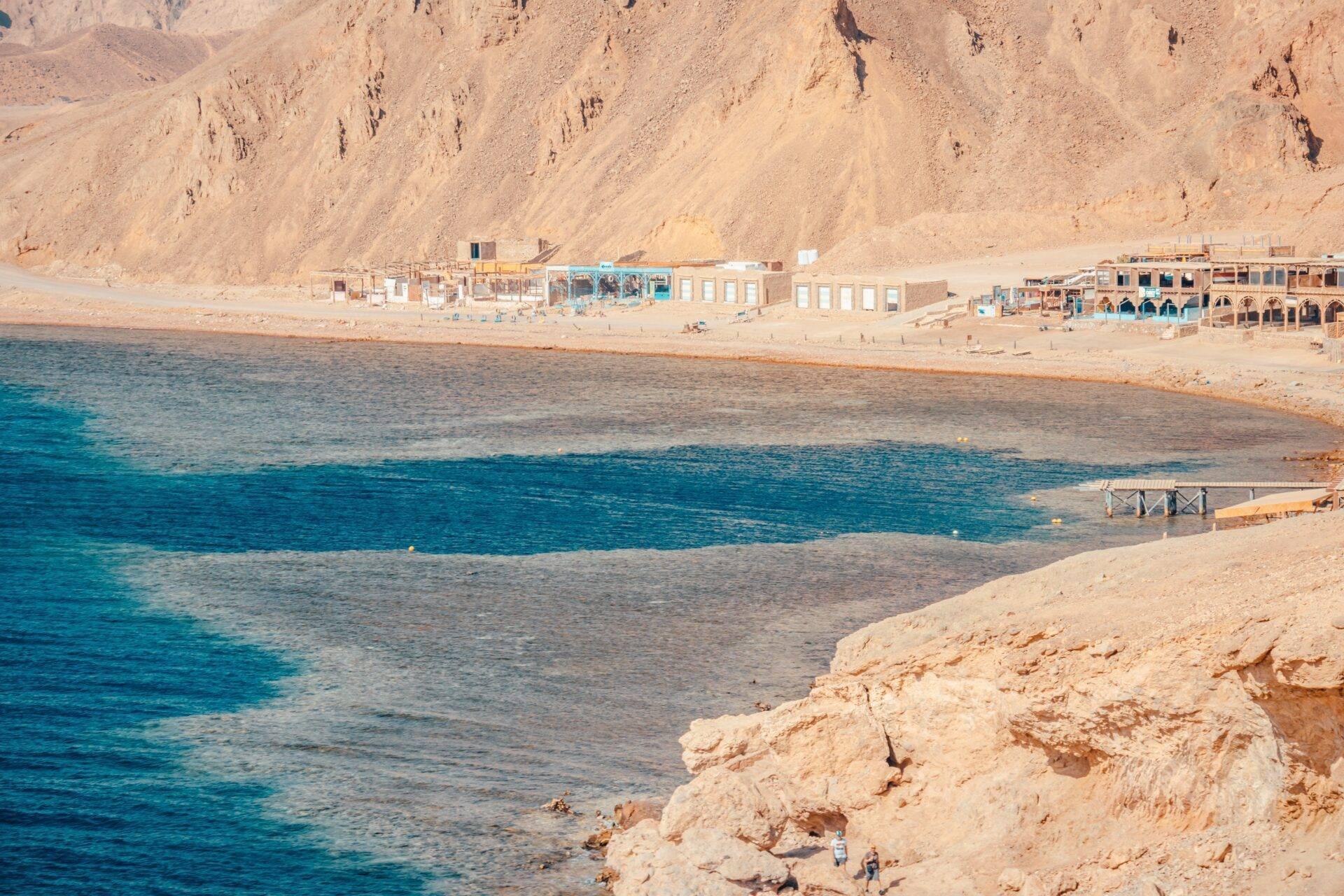 A quiet Egyptian beach with low coastal buildings, dry mountains and crystal-clear turquoise sea