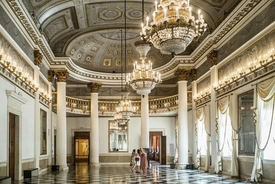 Grand palace hall with white columns, crystal chandeliers and a gilded ornamental ceiling