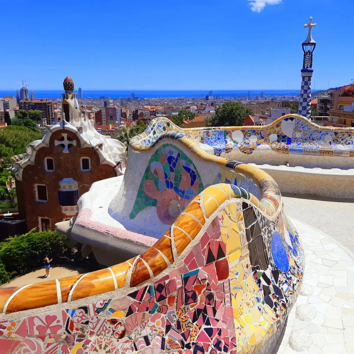 Vue panoramique d’un parc architectural coloré avec mosaïques, maisons fantaisistes et mer bleue en arrière-plan