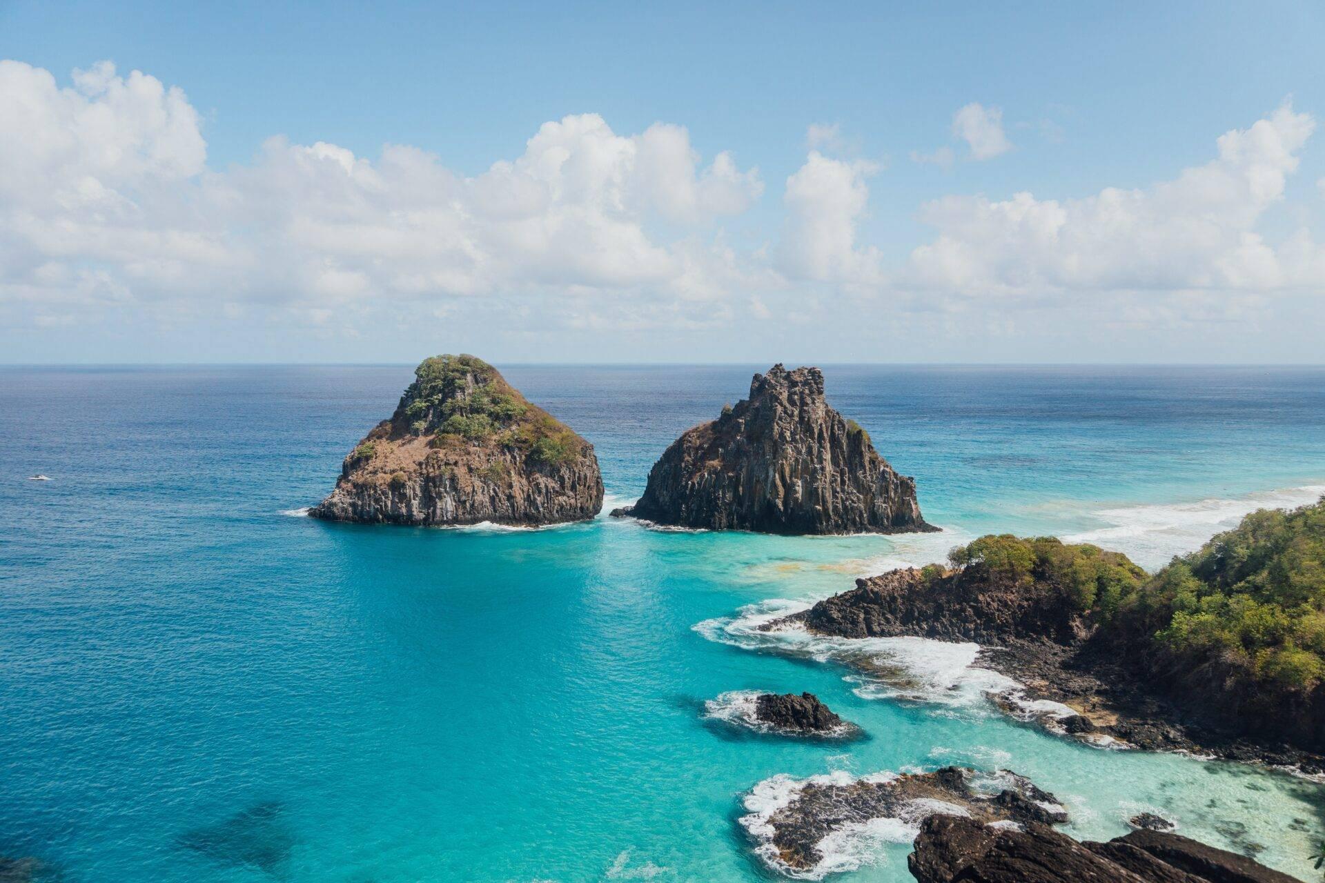 Dramatic rock formations rising from crystal-clear turquoise water, with a sandy beach and tropical vegetation