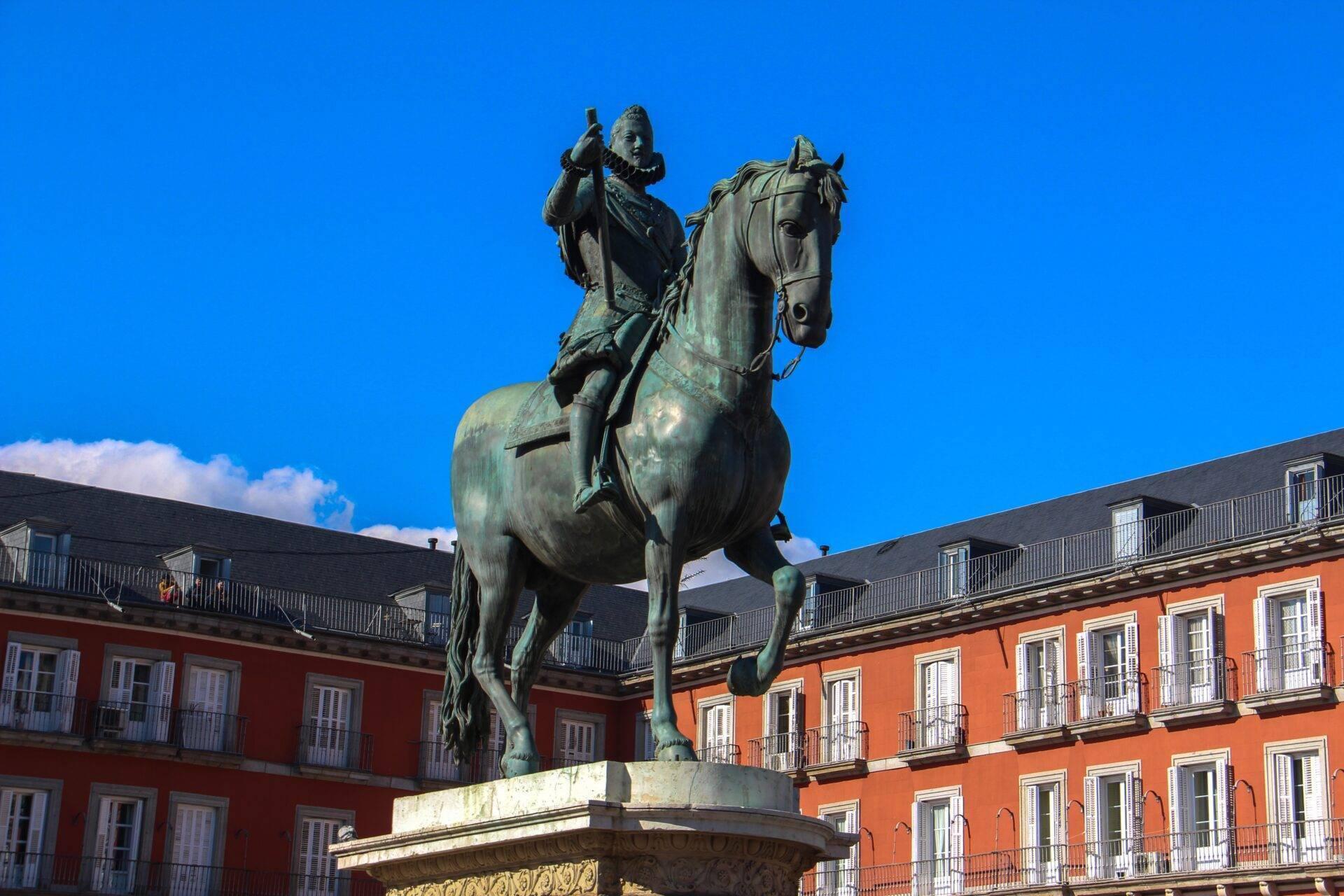 Statue équestre en bronze dans une plaza entourée de bâtiments coloniaux rouges sous ciel bleu