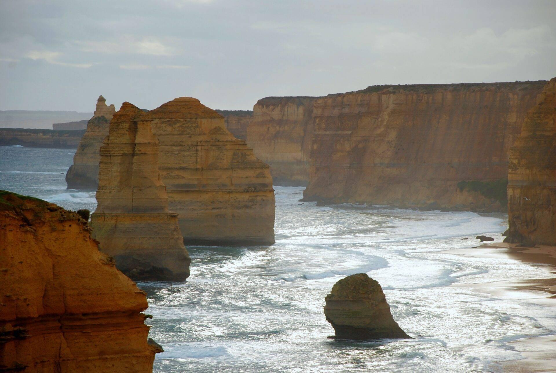 Imposantes formations rocheuses côtières émergeant de l’océan sous un ciel nuageux avec plage de sable