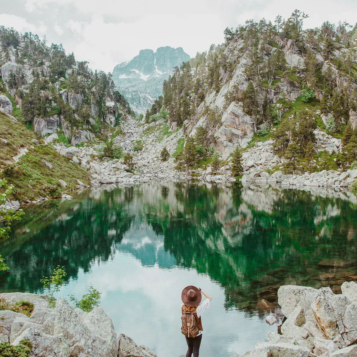 Une randonneuse contemplant un lac de montagne cristallin encadré de falaises rocheuses et de forêts de sapins