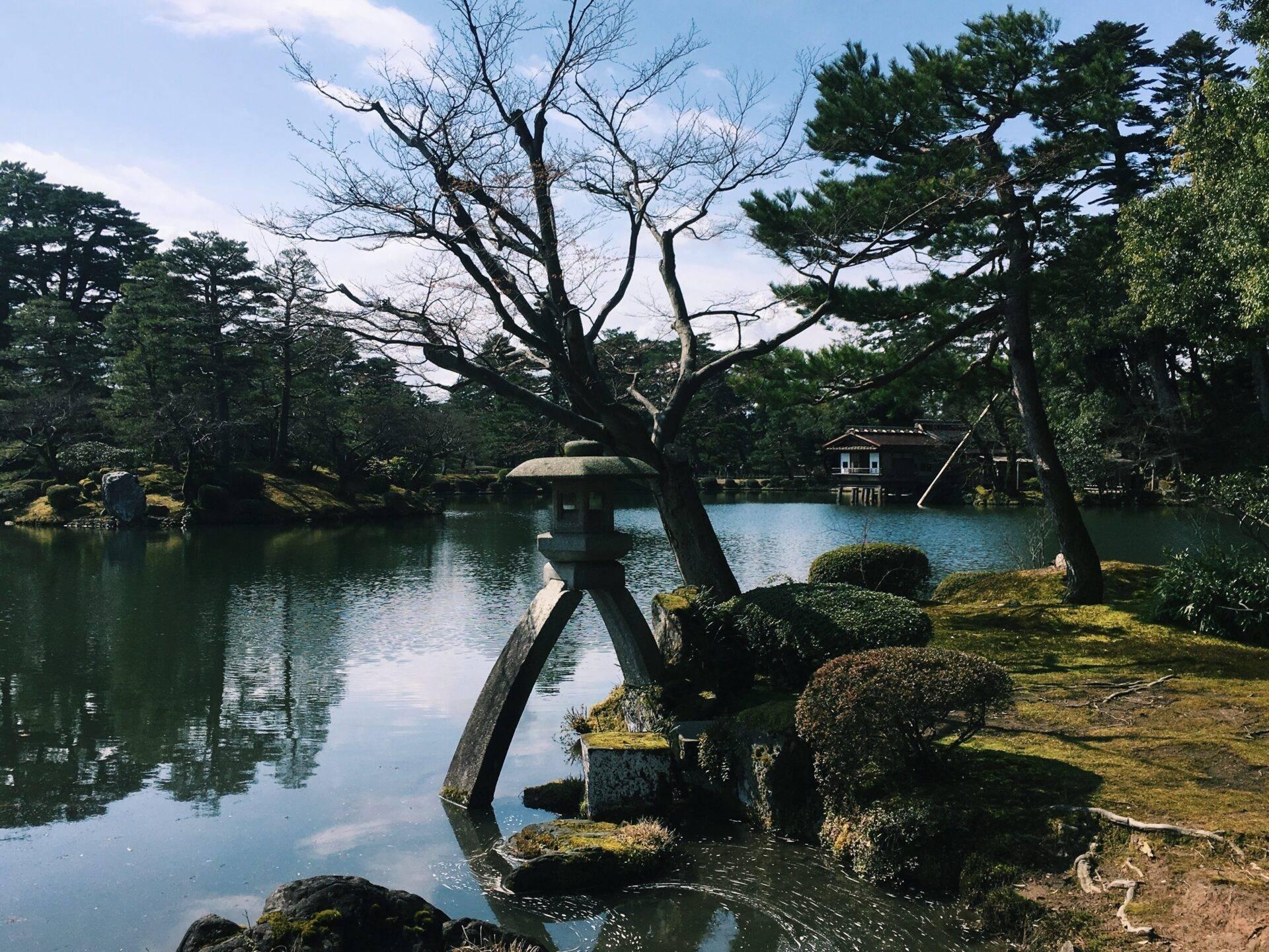 A traditional Japanese garden with a calm pond, ancient trees and a tea house at the water’s edge