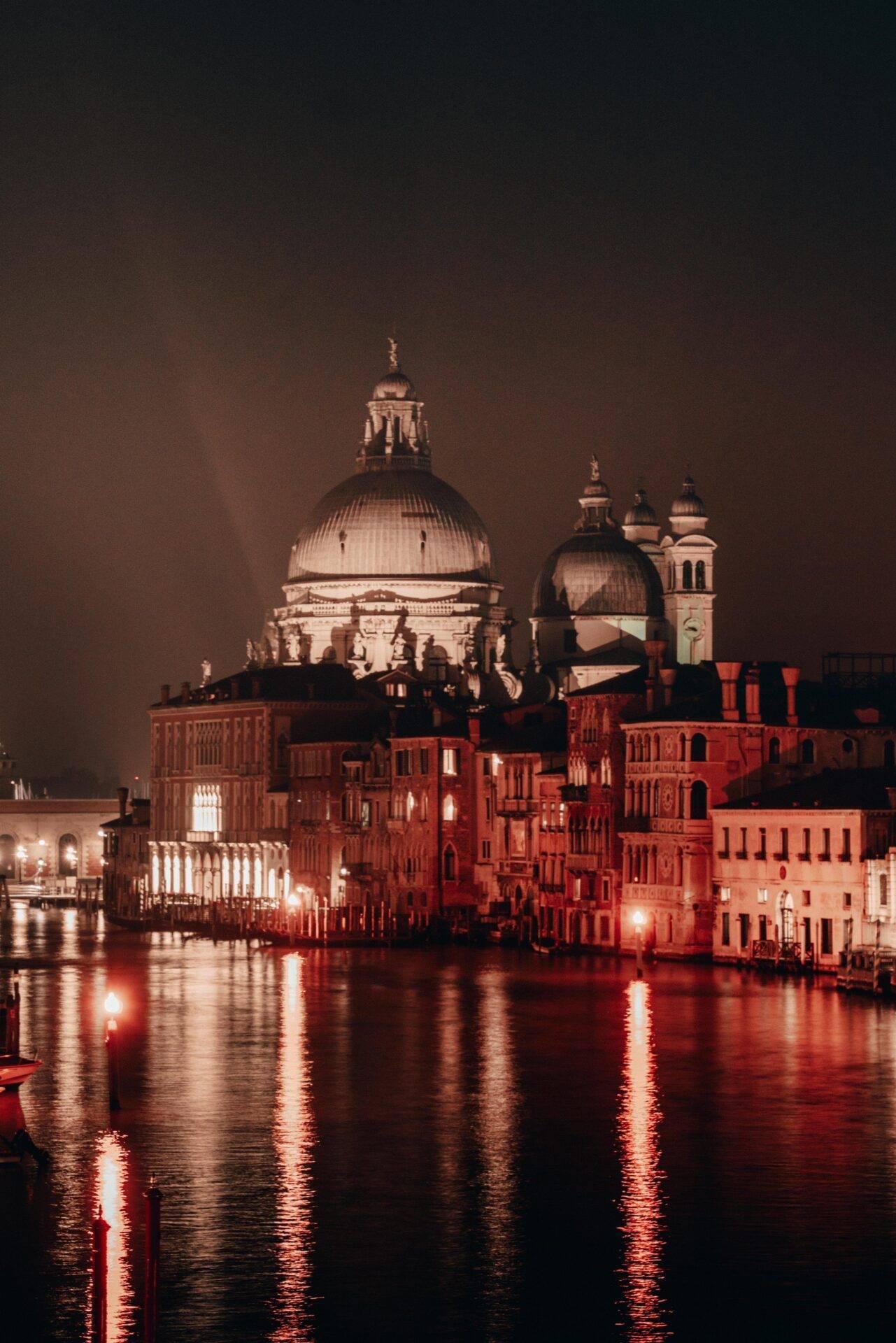 Night view of the illuminated Basilica della Salute above the Grand Canal with its red-brick historic buildings