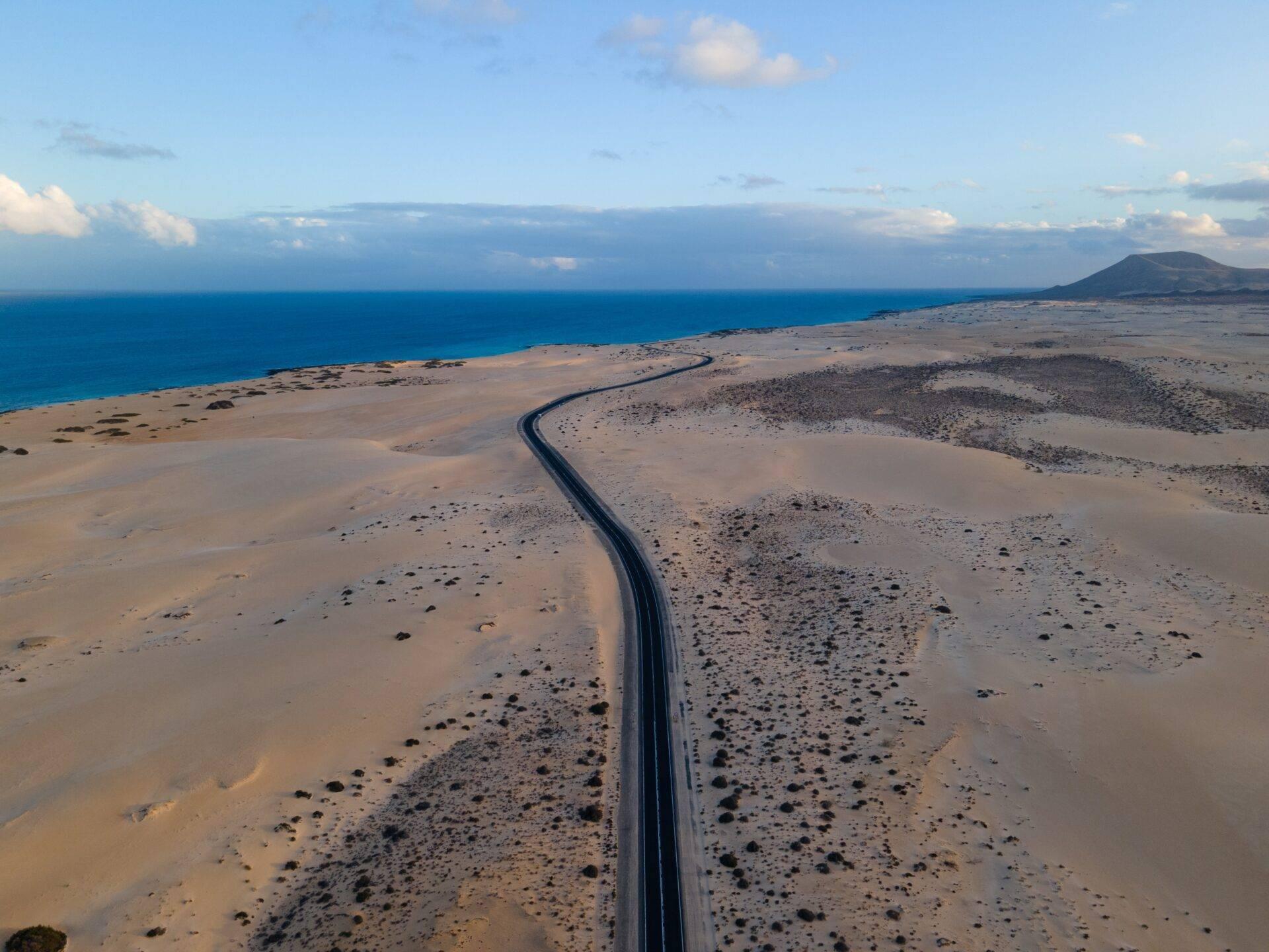 Route asphaltée traversant un paysage volcanique désertique vers la mer bleue et une île en arrière-plan