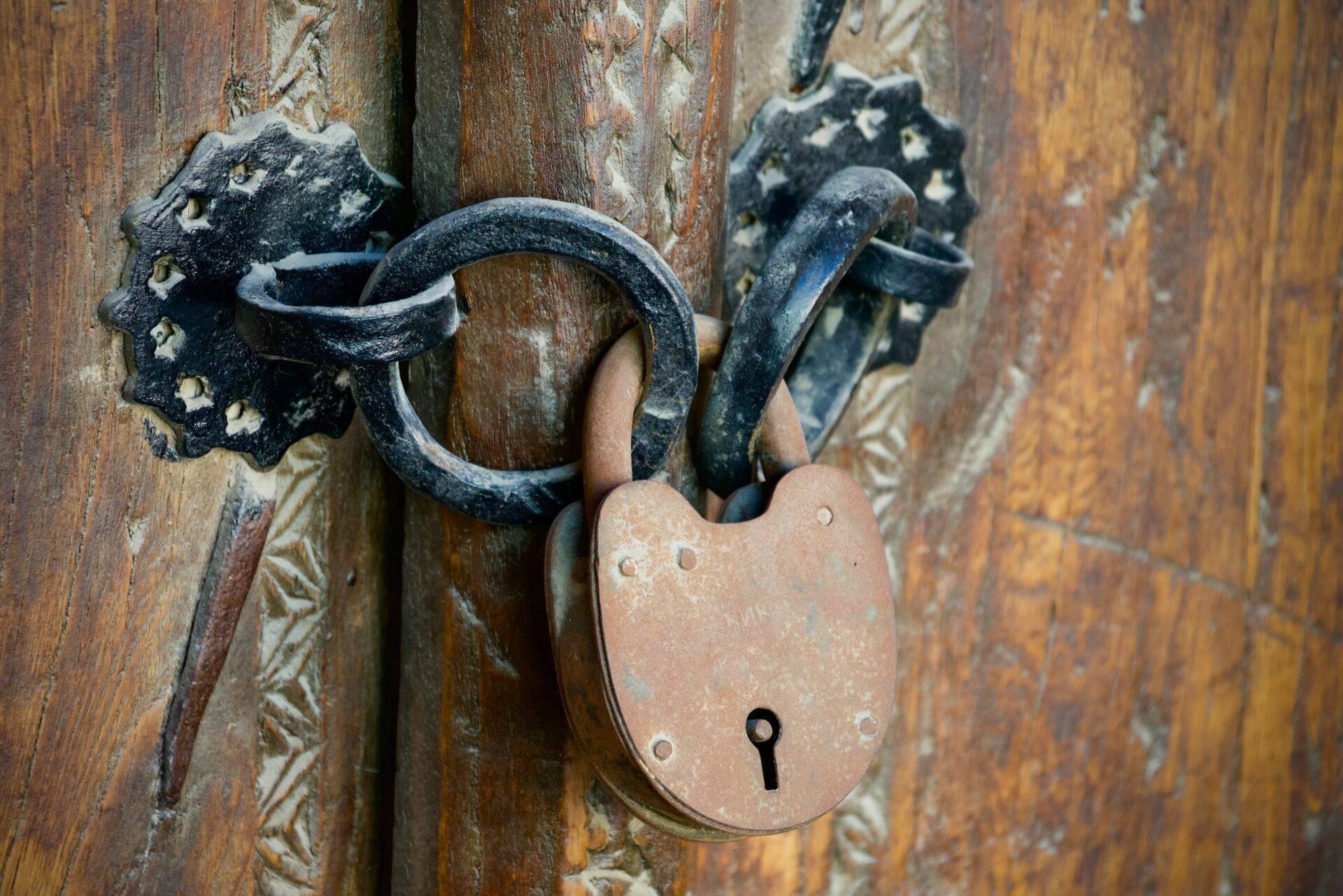An old copper padlock and a black ornamental forged lock on a worn wooden door