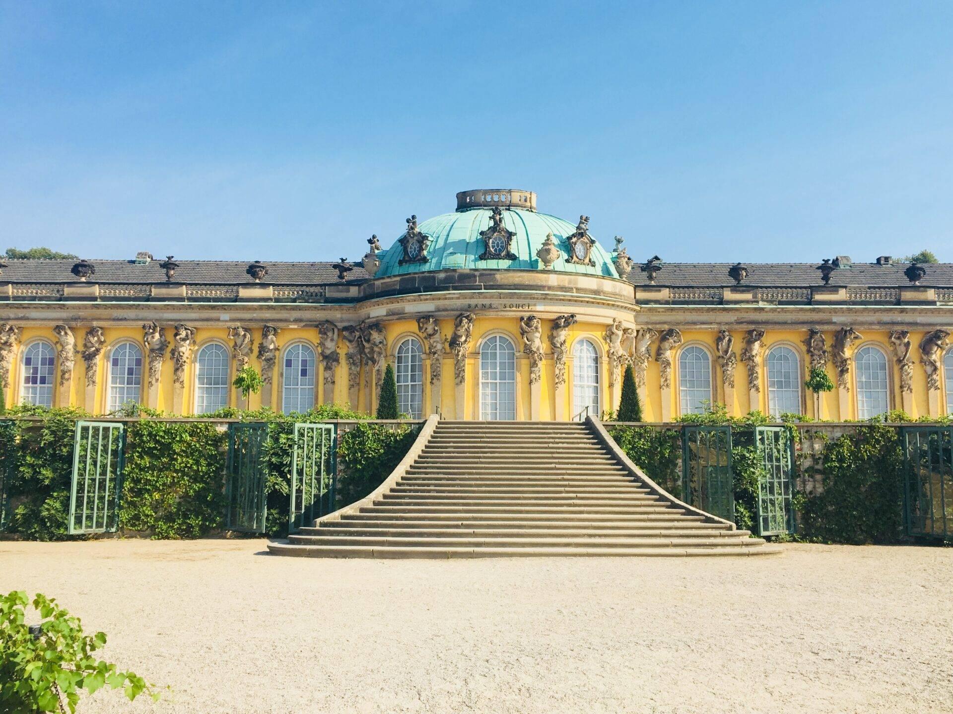 A yellow Baroque palace adorned with a turquoise-green dome and a grand stone staircase