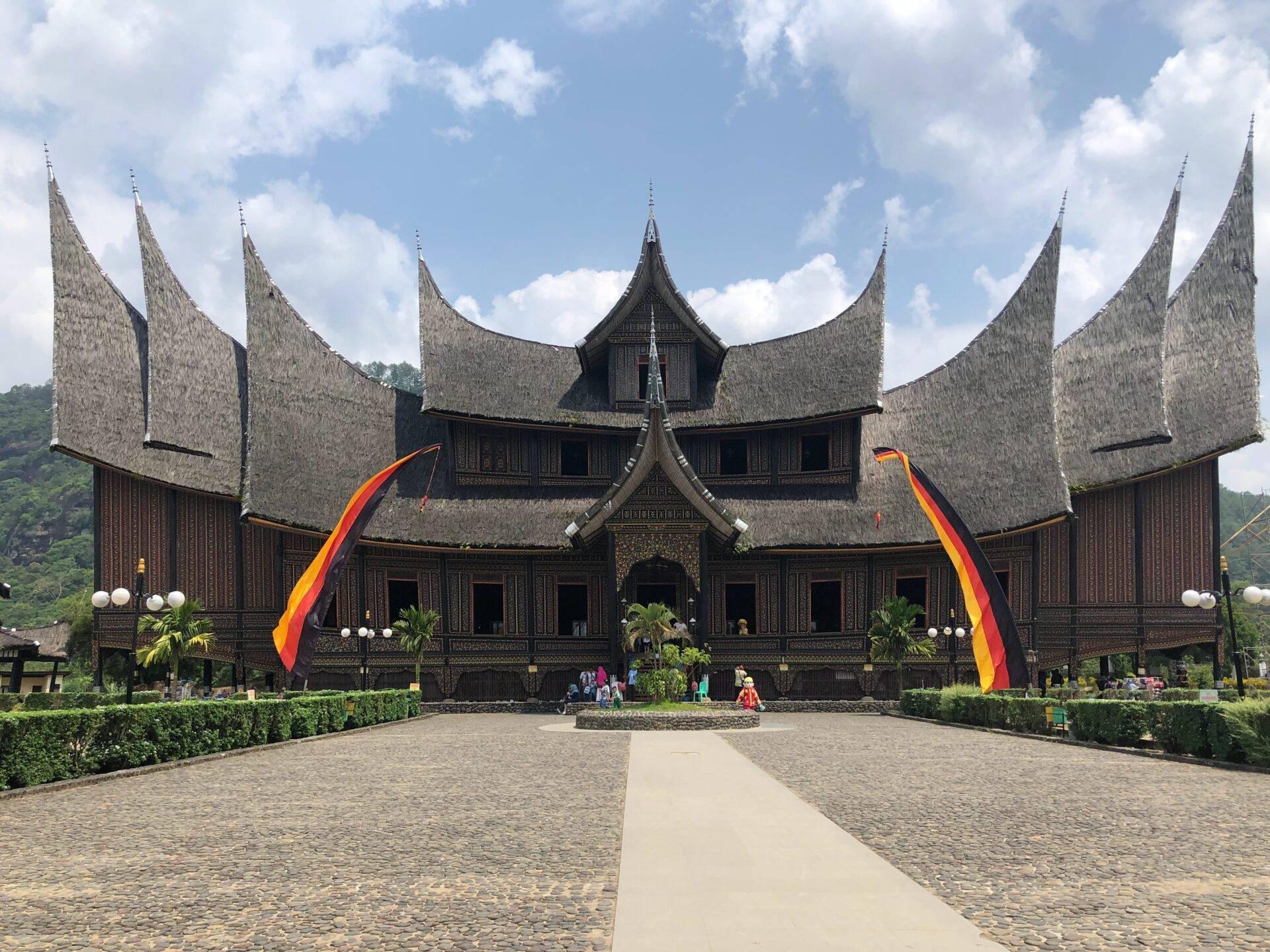 A traditional Indonesian temple with pointed thatched roofs and red and yellow flags under a blue sky