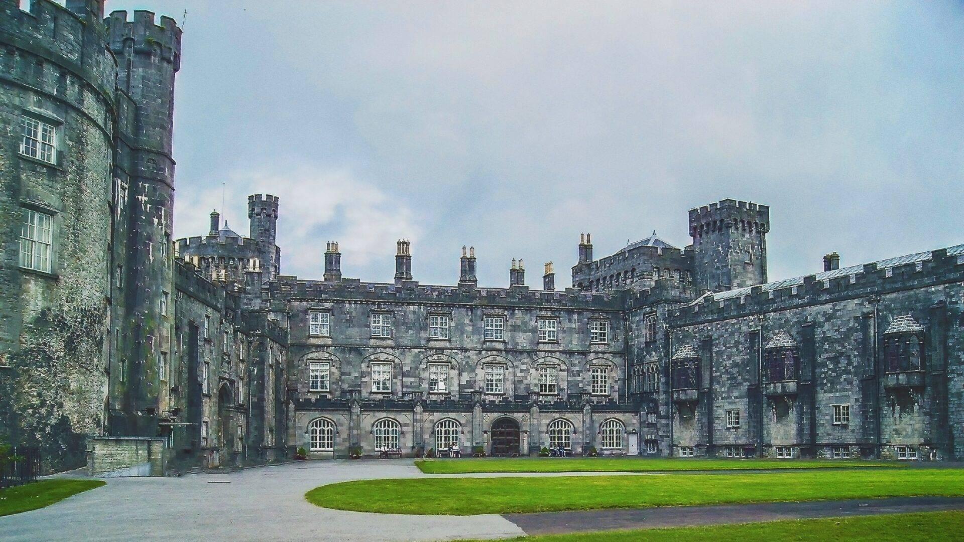 A grey-cobbled courtyard surrounded by grey stone buildings with battlements and towers typical of an Irish medieval fortress