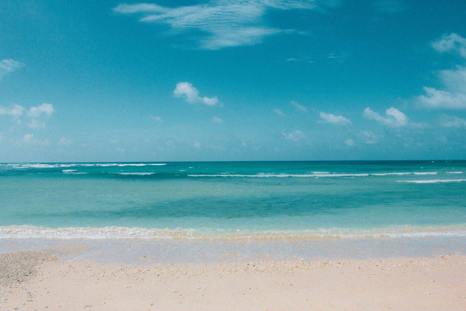 Plage de sable blanc avec eaux turquoise cristallines et ciel bleu dégagé, incarnant un paradis tropical idéal