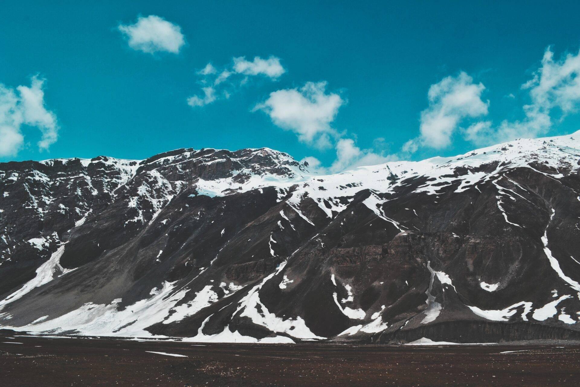 Snow-capped mountain range with black rocky slopes and a clear blue sky, dramatic alpine desert landscape