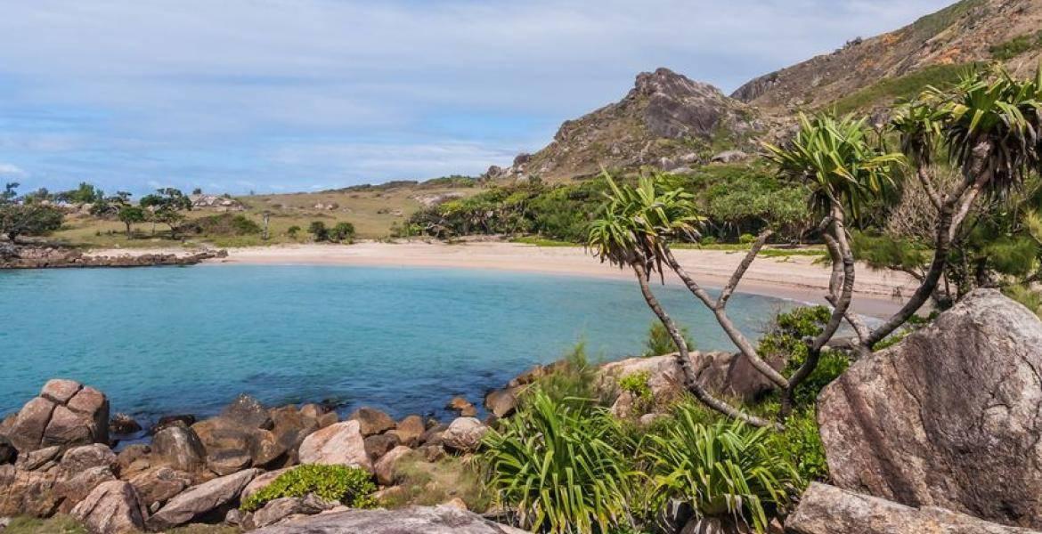 A tropical bay with turquoise water bordered by a white sandy beach, granite rocks and lush green vegetation