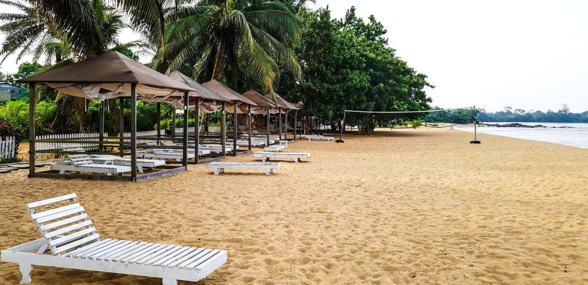 Plage de sable avec chaises longues blanches et abris couverts sous palmiers en bord de mer