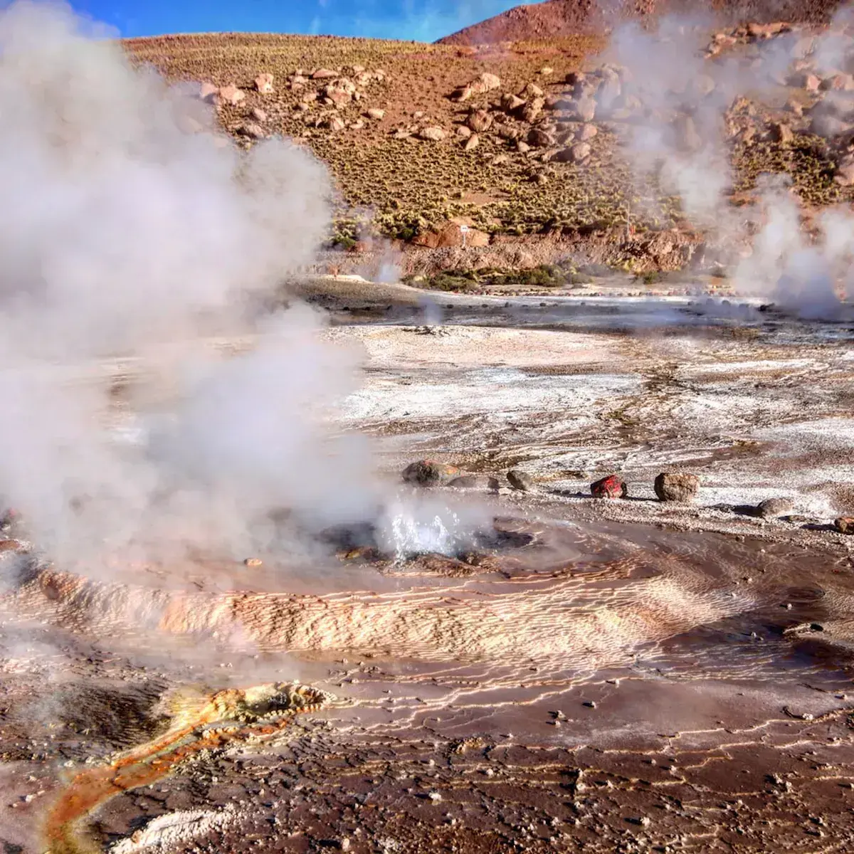Steaming geysers and hot springs in a mountainous desert landscape with colourful mineral deposits