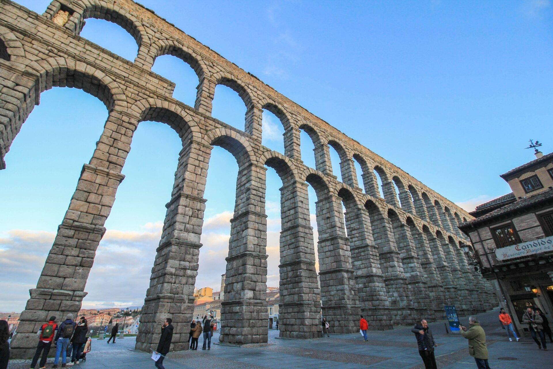 L’aqueduc romain de Ségovie avec ses arches de pierre monumentales et des visiteurs flânant sur la place