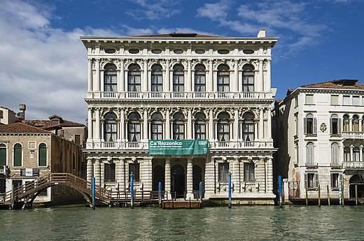 A white Venetian palazzo with ornate facades overlooking the Grand Canal under a clear blue sky