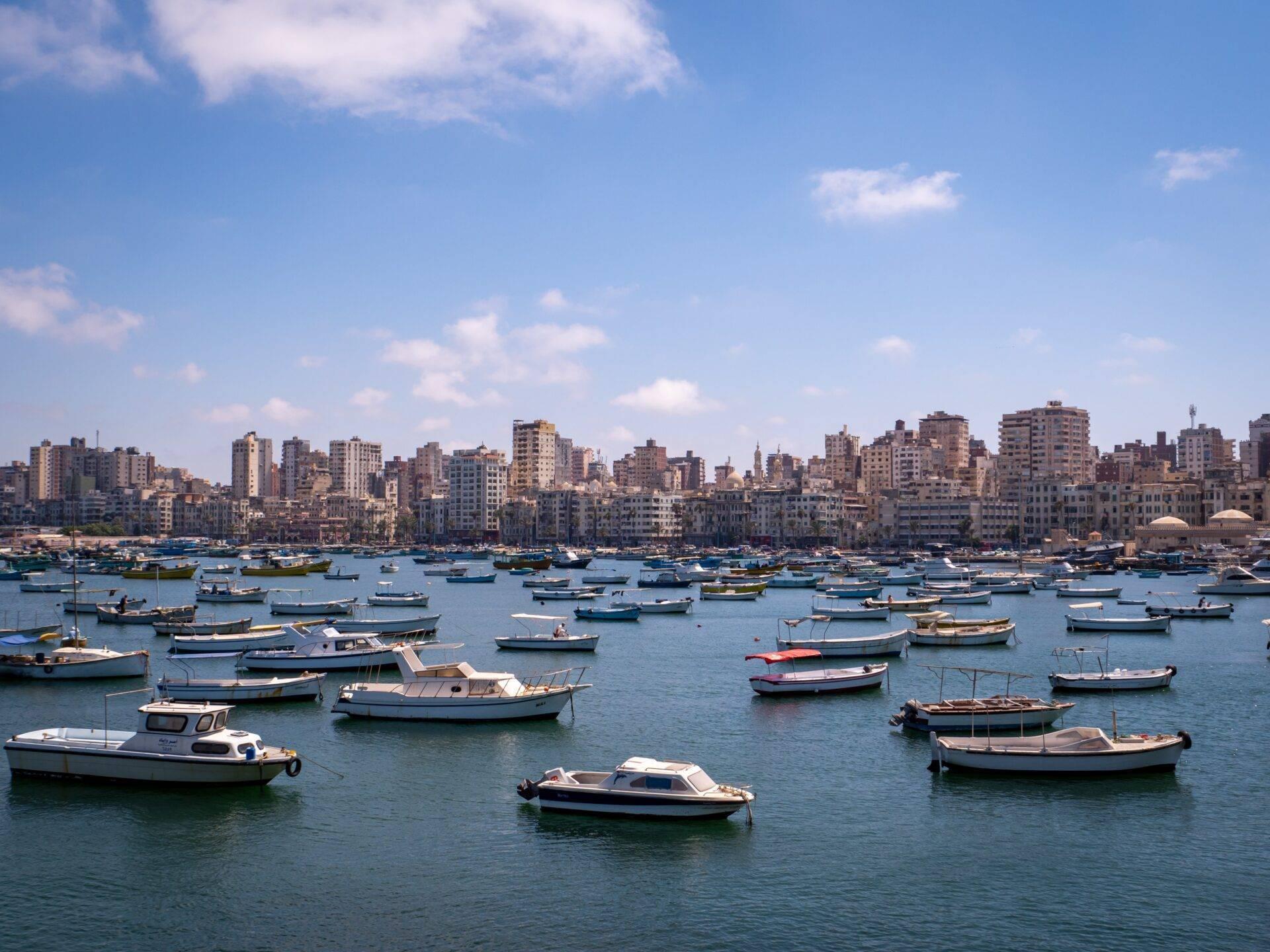 A Mediterranean coastal bay with dozens of small fishing boats and a vast densely built city skyline in the background