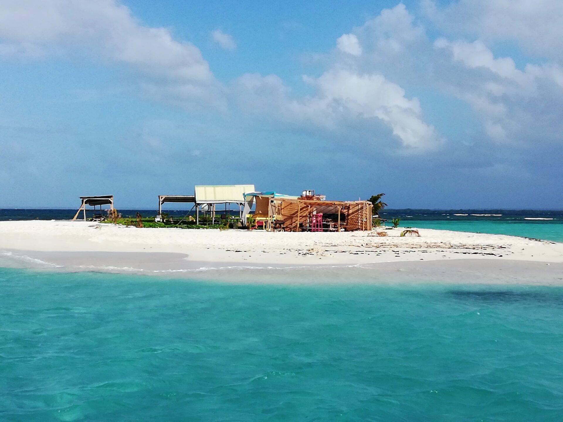 Une plage tropicale déserte avec cabanes en bois, turquoise cristalline et ciel bleu nuageux