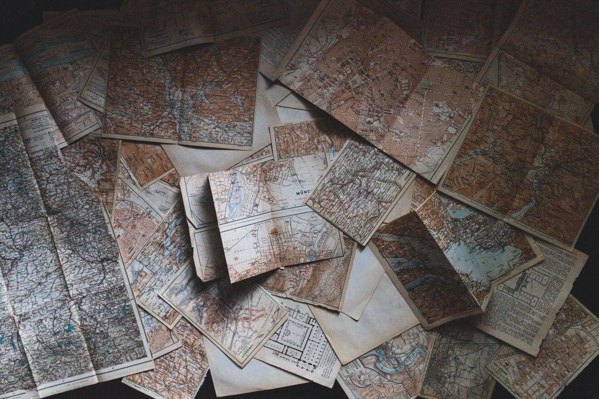 Collection of antique geographical maps and city plans spread on a white surface, evoking the spirit of exploration