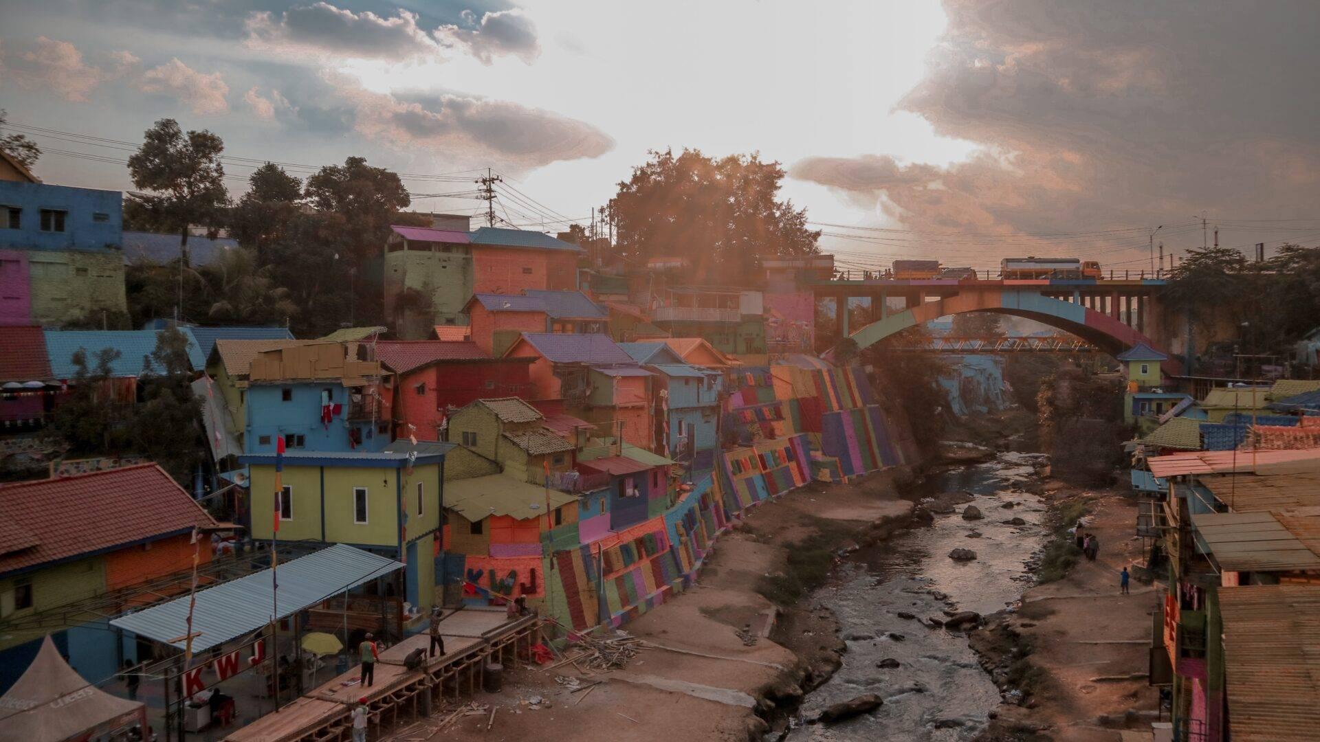 A colourful riverside village with brightly painted houses, a bridge and a cloudy sky