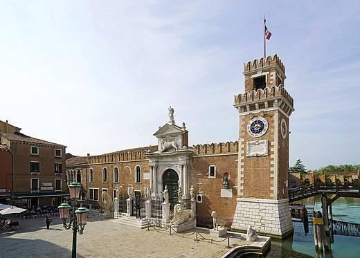 A historic Venetian square with a brick clock tower and a classical stone building beside a canal