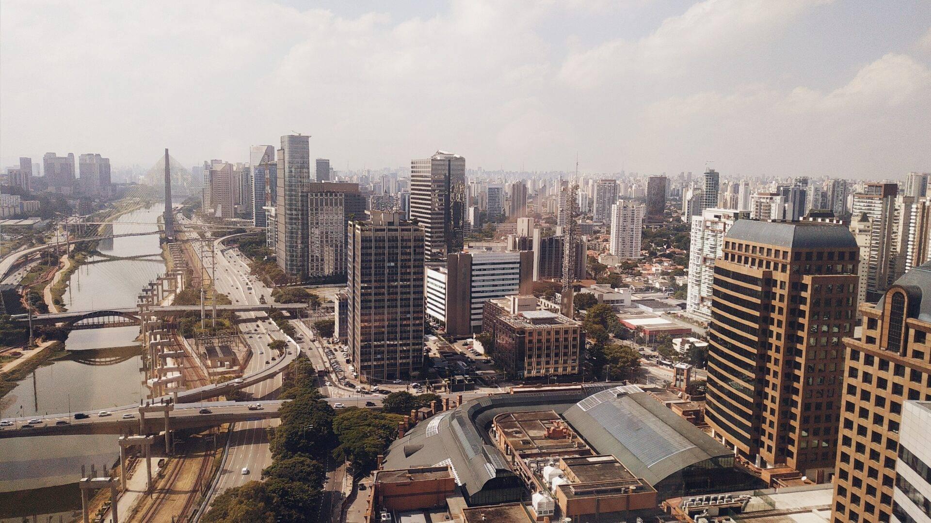 Aerial view of a Brazilian metropolis with skyscrapers, a river, bridges and dense urban architecture under a cloudy sky