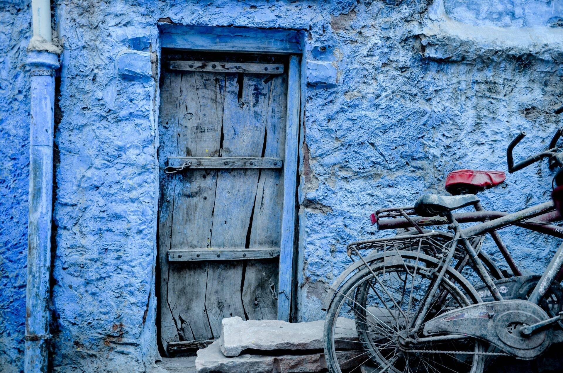 Blue wooden door on a painted wall in an old city, with a rusty bicycle leaning against it