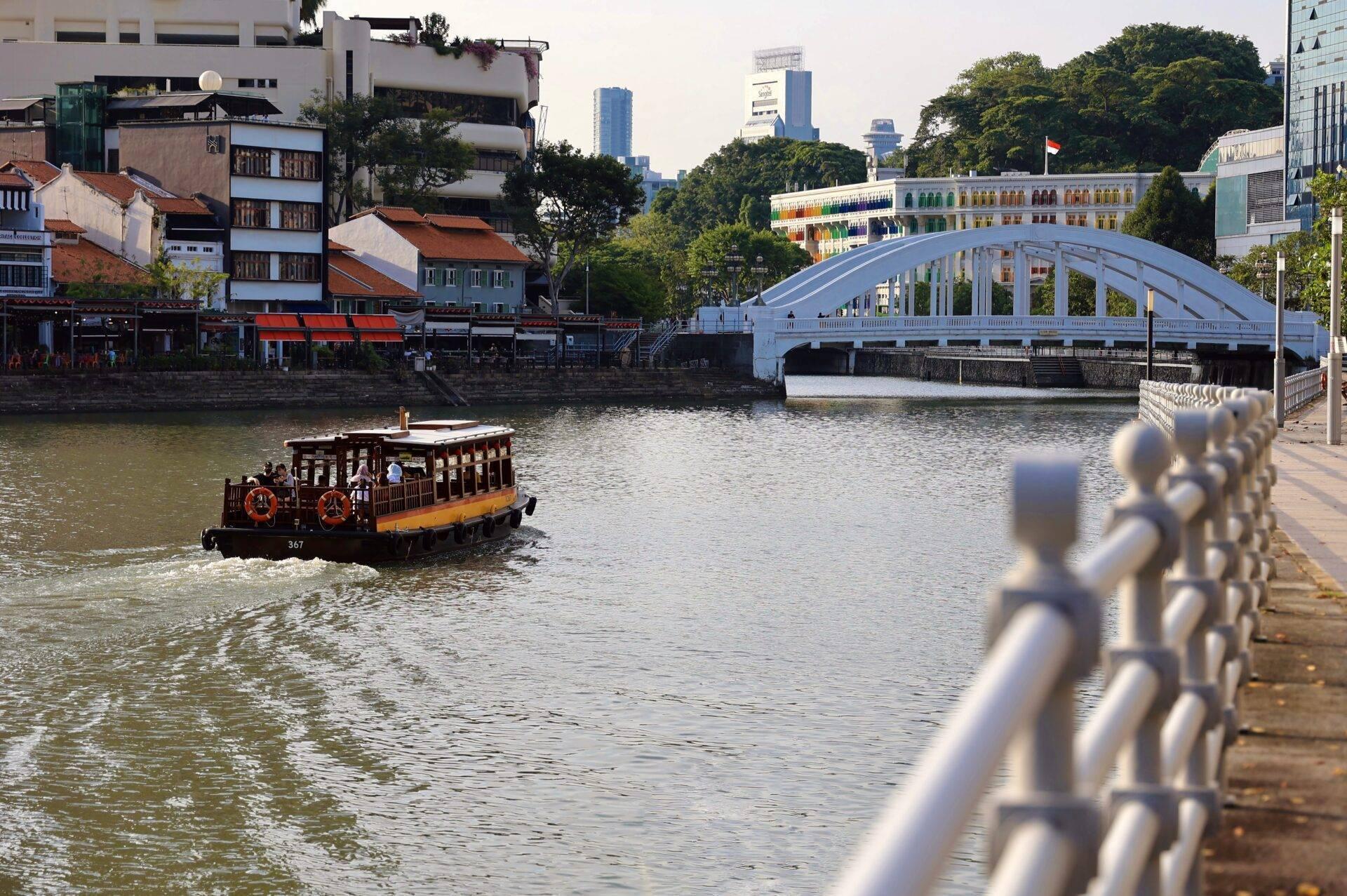 Un bateau touristique navigue sur une rivière urbaine devant un pont blanc arqué et des bâtiments colorés