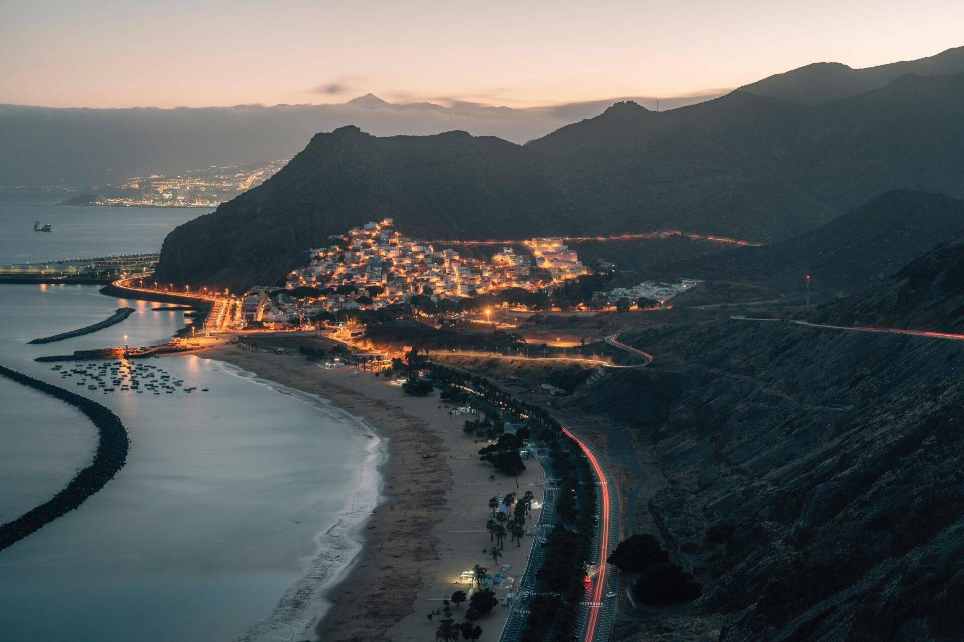 Vue aérienne au crépuscule d’une petite ville côtière illuminée encadrée par des montagnes et la mer